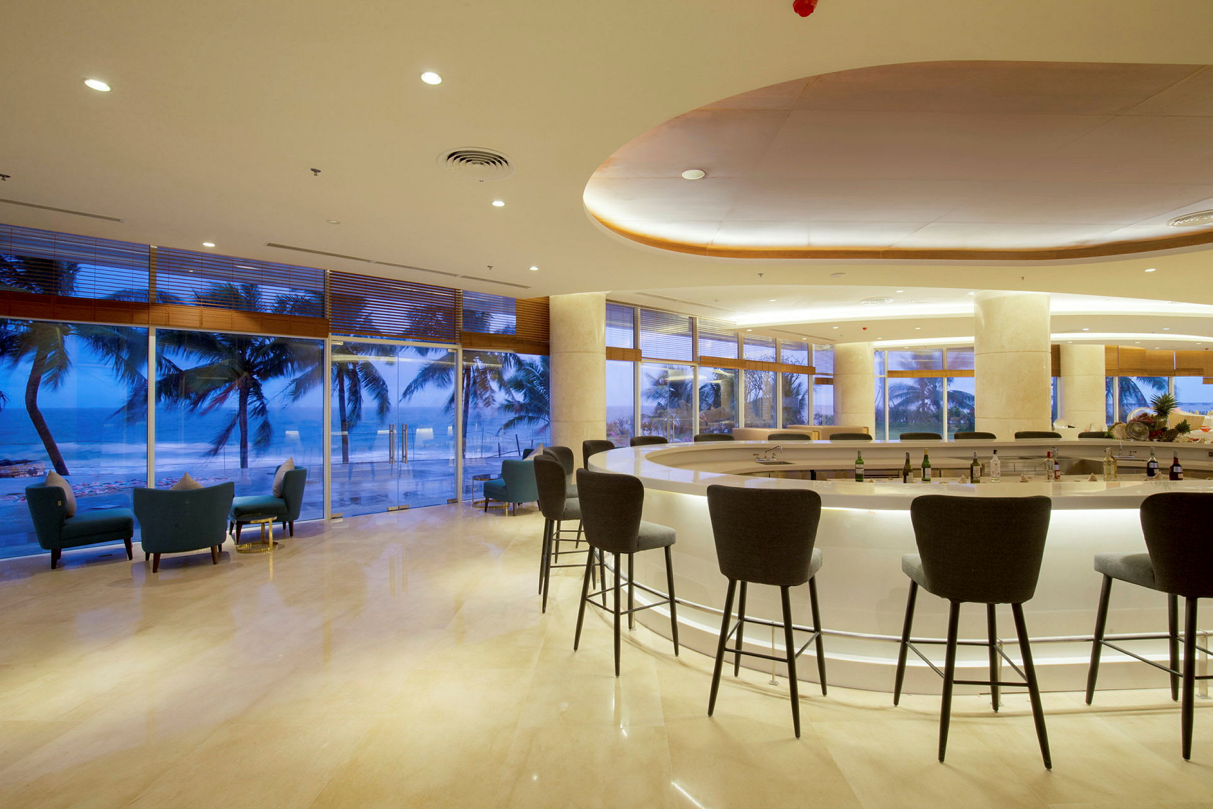 Interiör av en bar med höga stolar och glasfönster med utsikt över palmer och hav. (AI-genererad text)