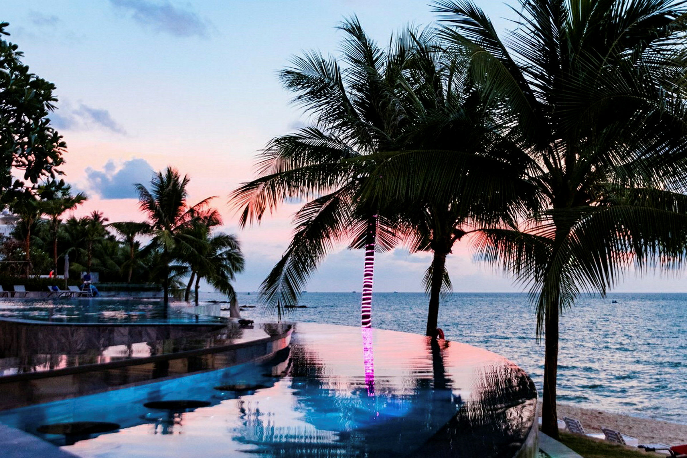 En infinitypool med palmer och havet i bakgrunden, vid solnedgång. (AI-genererad text)