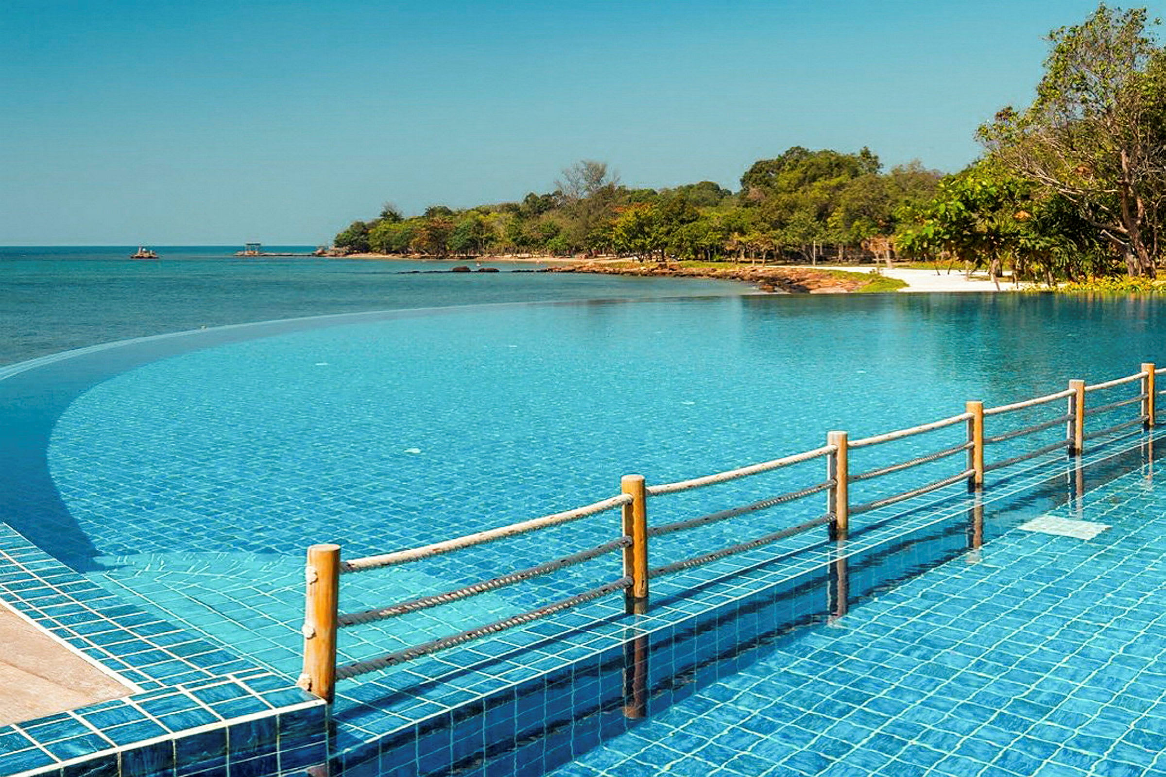 En infinitypool vid en kust med klarblått vatten och omgivande grönska. (AI-genererad text)