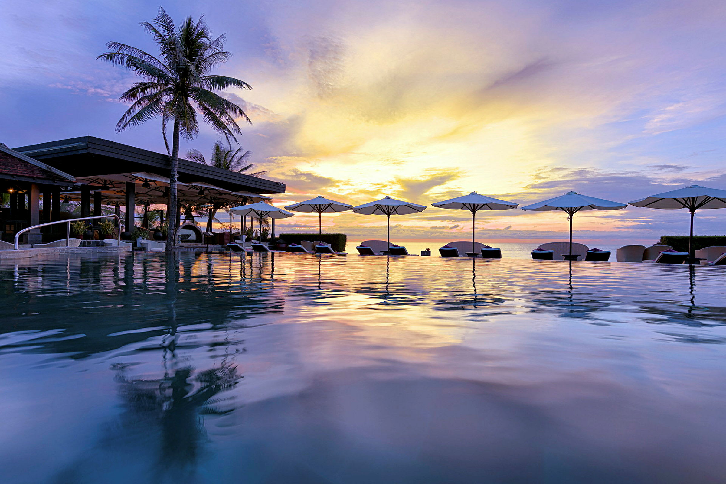 En infinitypool med solstolar och parasoller vid en tropisk resort, med en solnedgång som lyser upp himlen. (AI-genererad text)