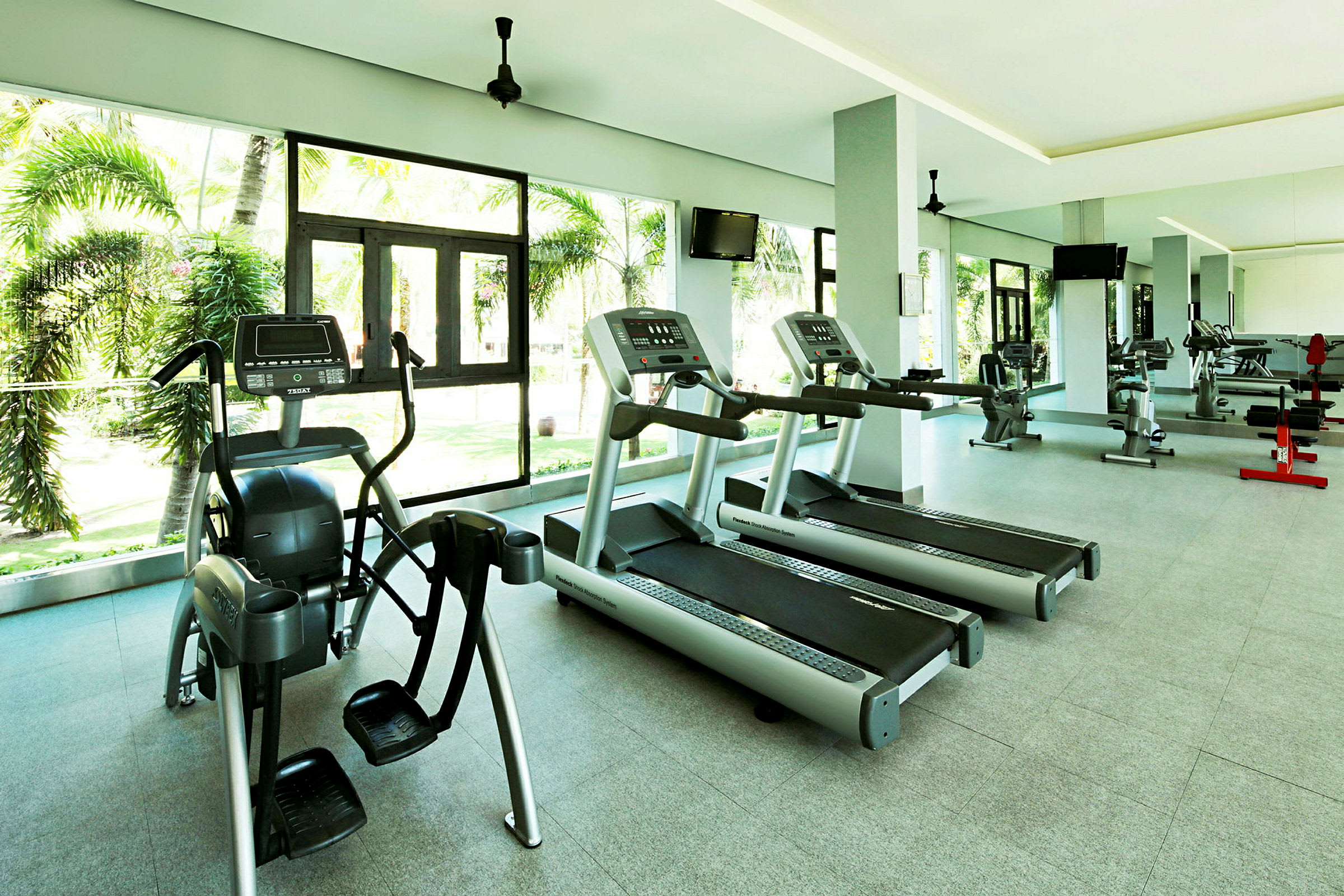 Gym med träningsmaskiner och stora fönster som vetter mot palmer utanför. (AI-genererad text)