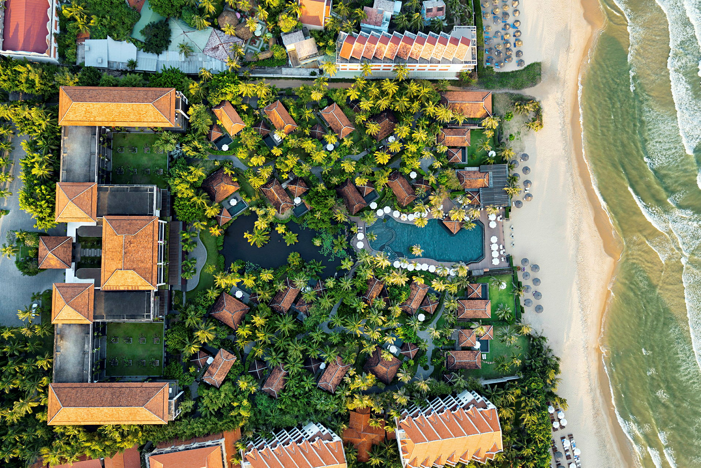 Flygbild över tropiskt hotellområde med träd, pool och strand. (AI-genererad text)