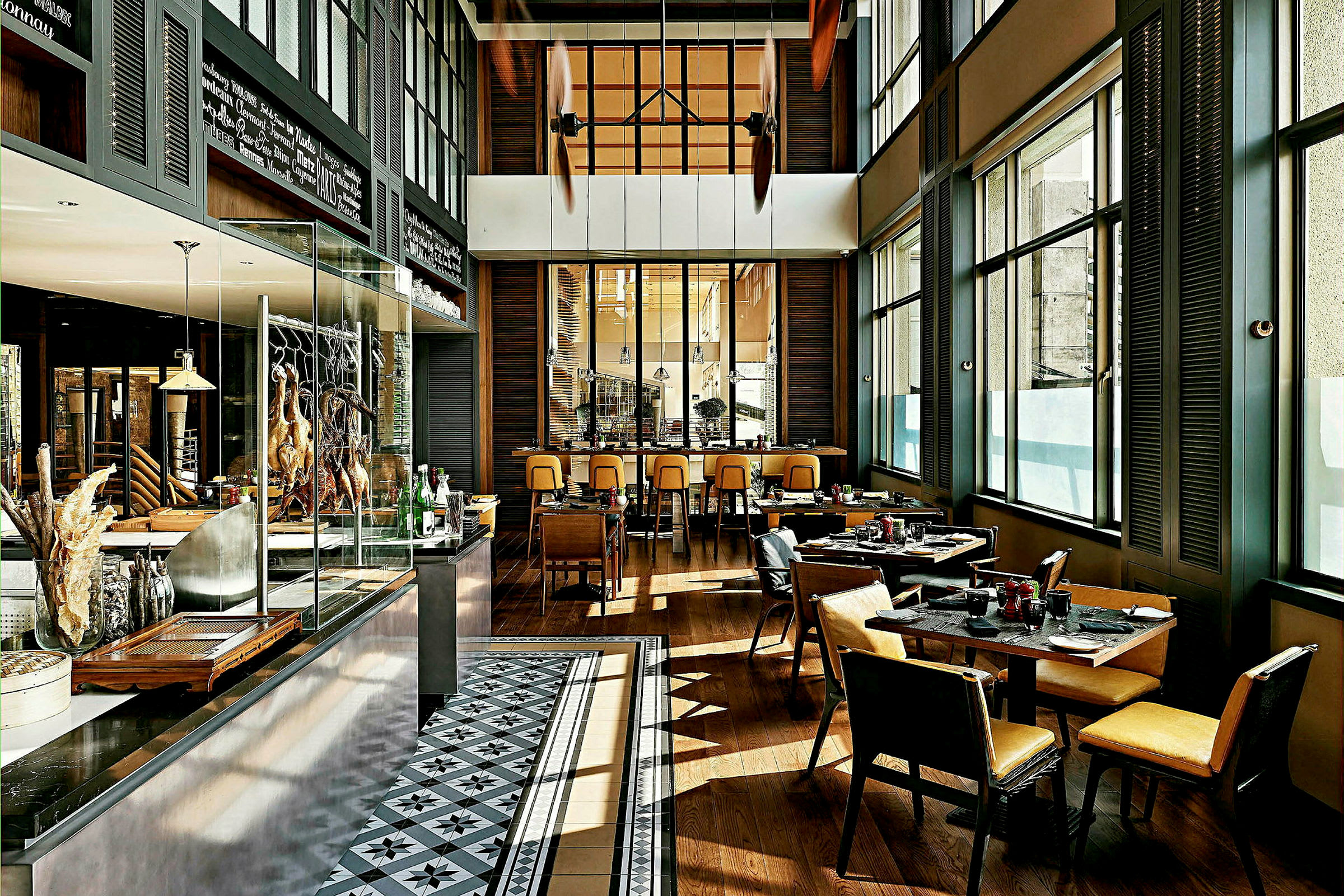 Interiör av en modern restaurang med bord och stolar, stora fönster och ett öppet köksområde. (AI-genererad text)