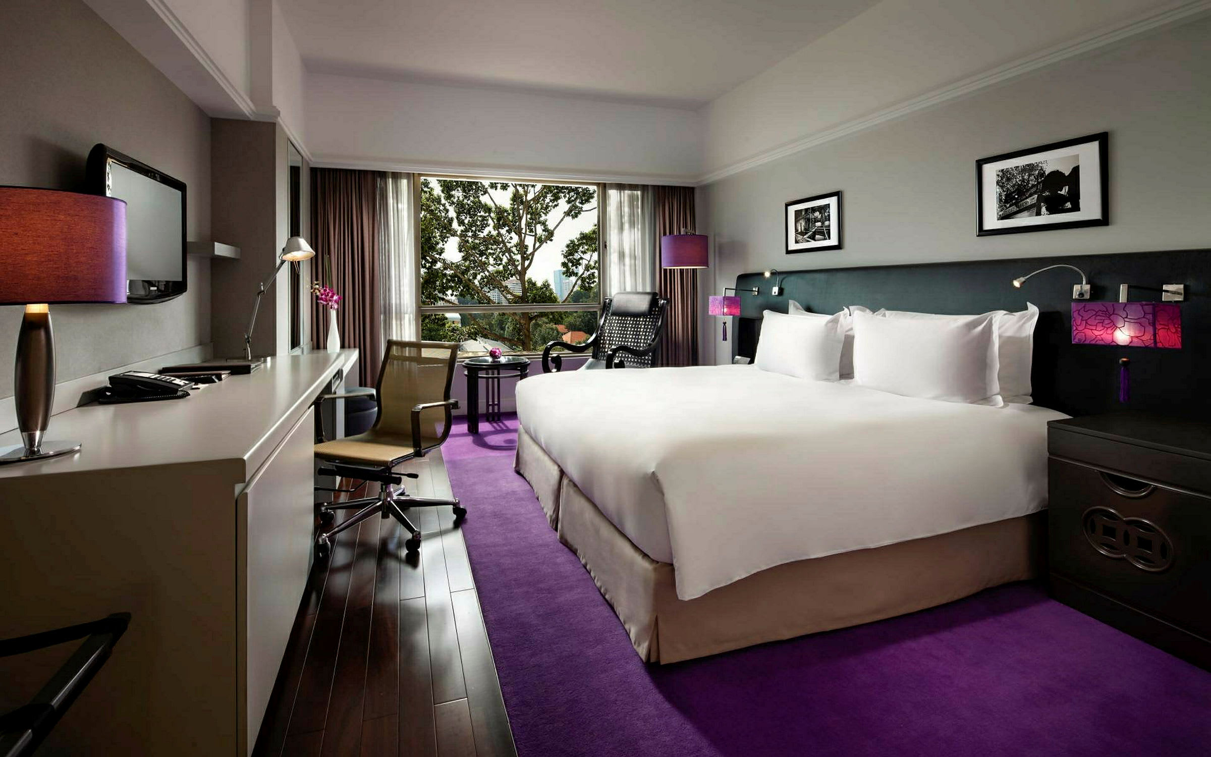 Hotellrum med en stor säng och modern inredning, skrivbord och stol samt en utsikt genom ett stort fönster. (AI-genererad text)