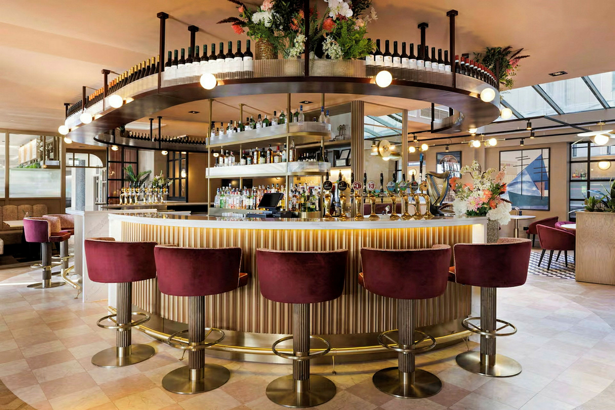 En elegant bar med vinflaskor på hyllor, blomarrangemang och sittplatser med röda sammetsstolar. (AI-genererad text)