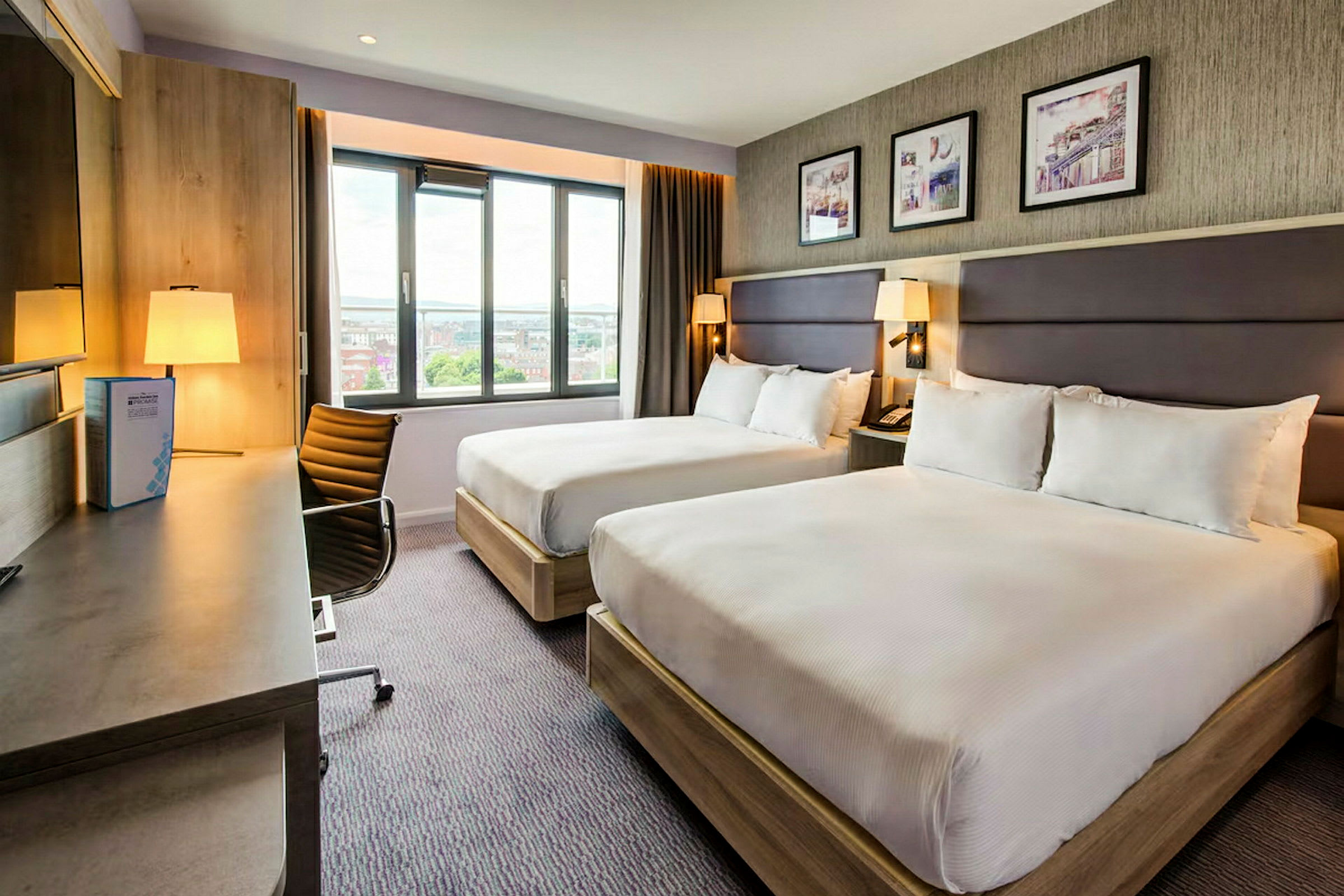 Hotellrum med två sängar, skrivbord och fönster. (AI-genererad text)