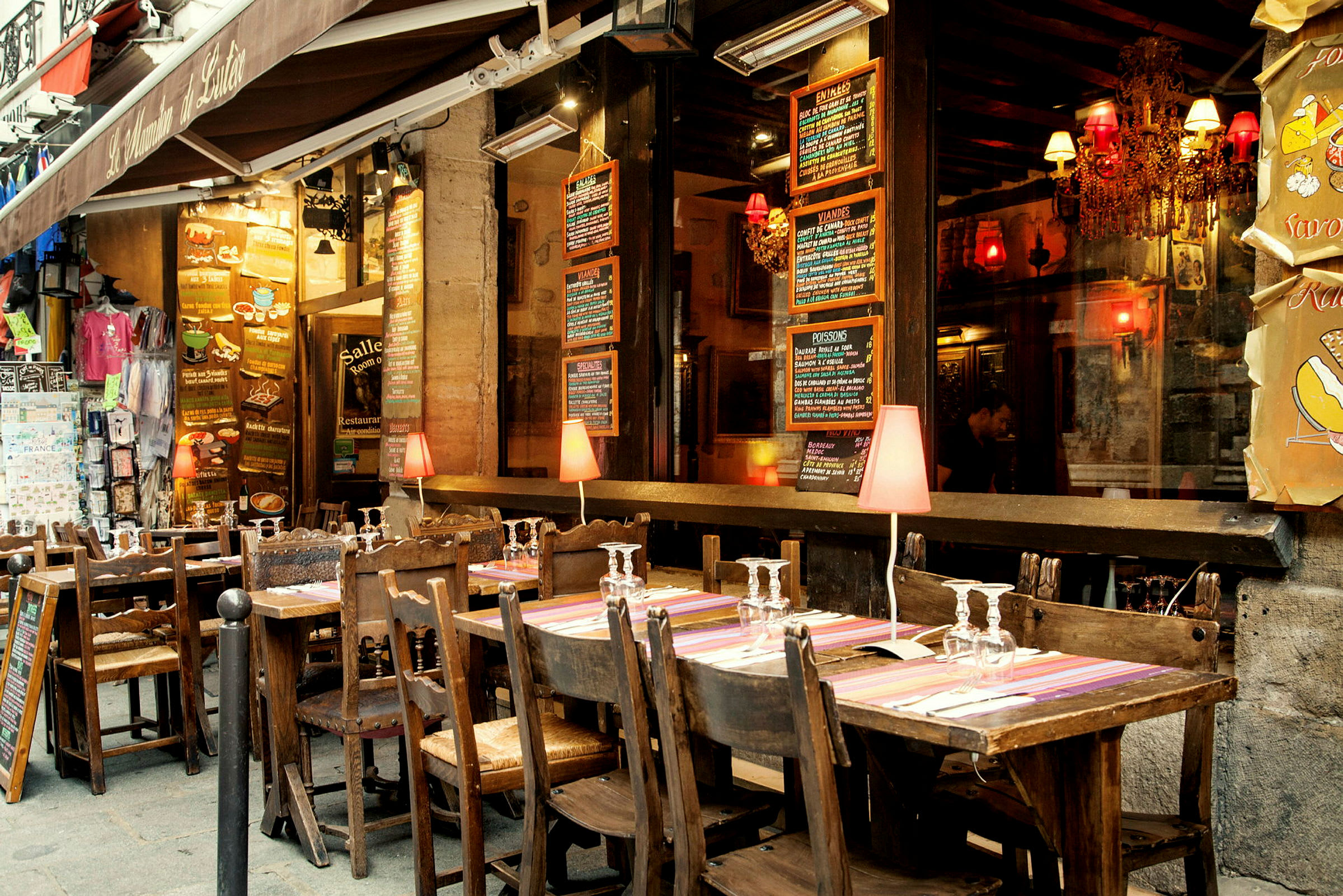 En uteservering med trämöbler framför en restaurang med meny-tavlor. (AI-genererad text)