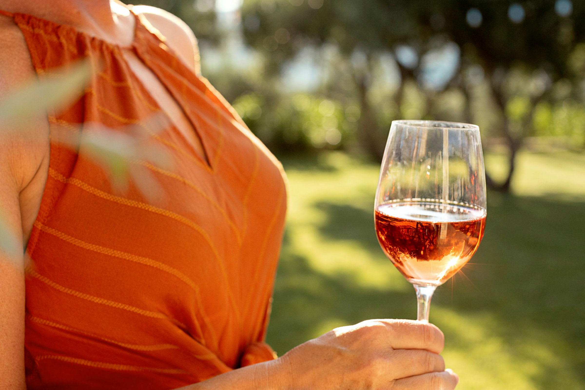 En person håller i ett glas rosévin utomhus. (AI-genererad text)