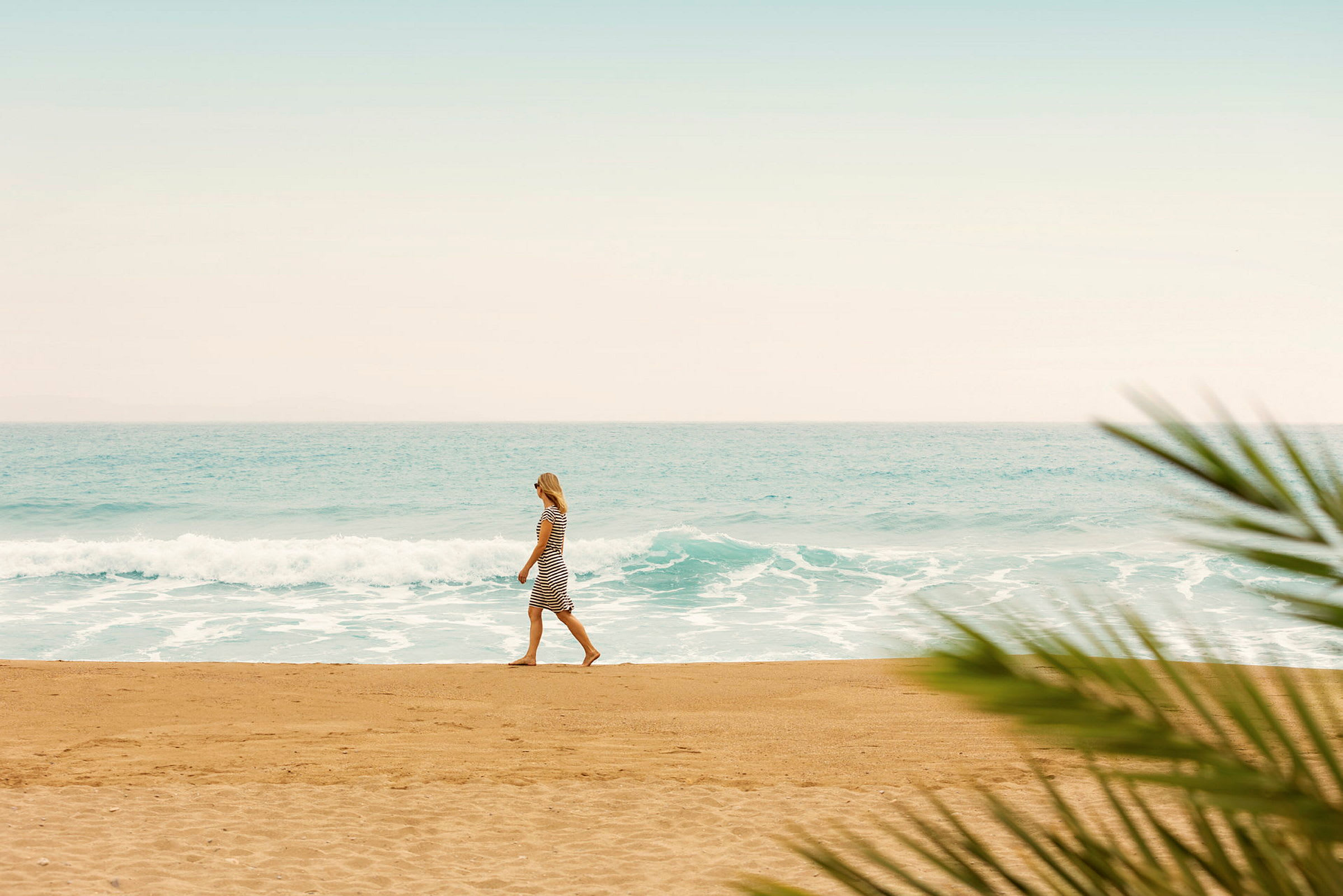 En person promenerar på en sandstrand med havet och vågor i bakgrunden. (AI-genererad text)