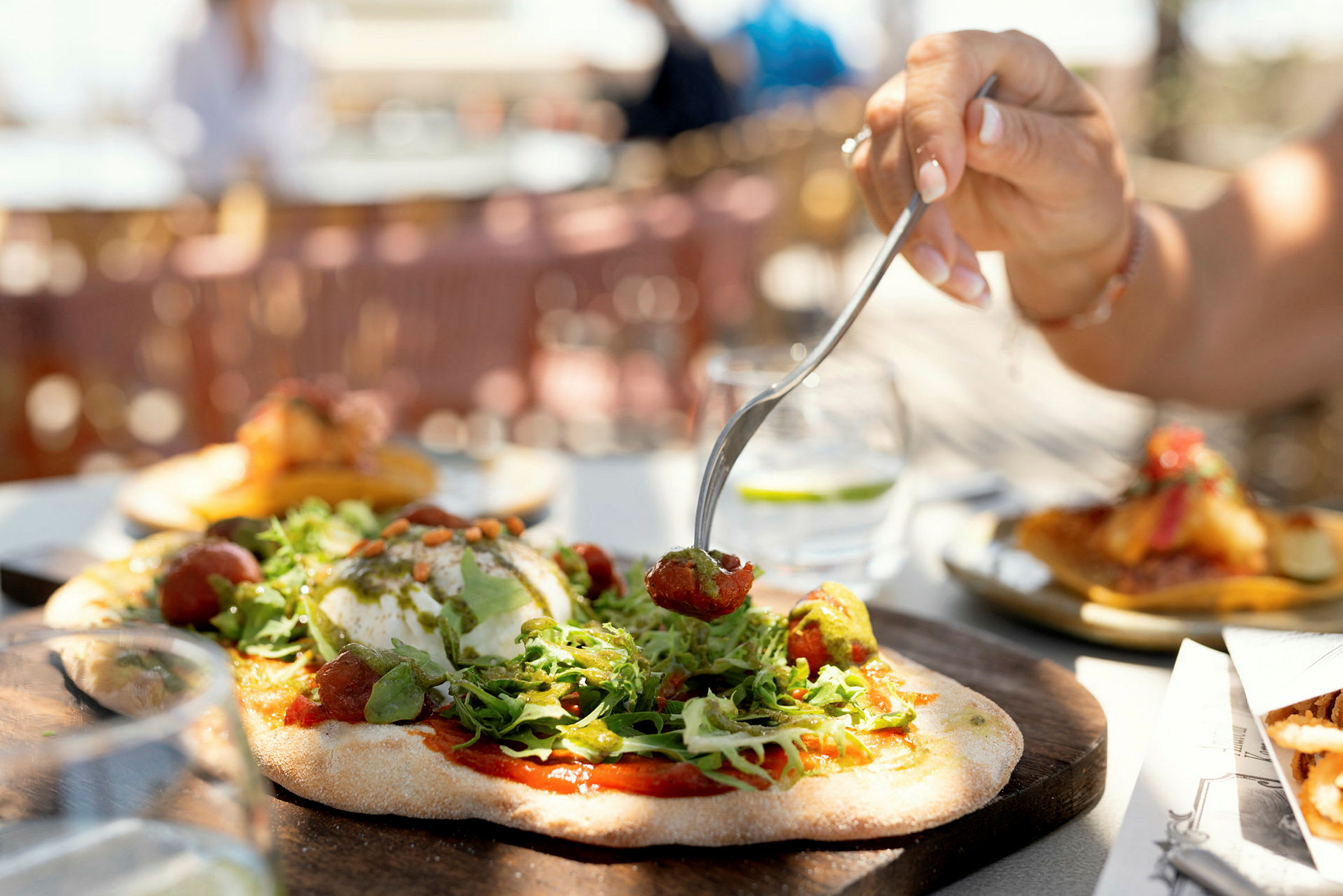 En hand använder en gaffel för att plocka upp mat från en pizza, med sallad och tillbehör på. (AI-genererad text)