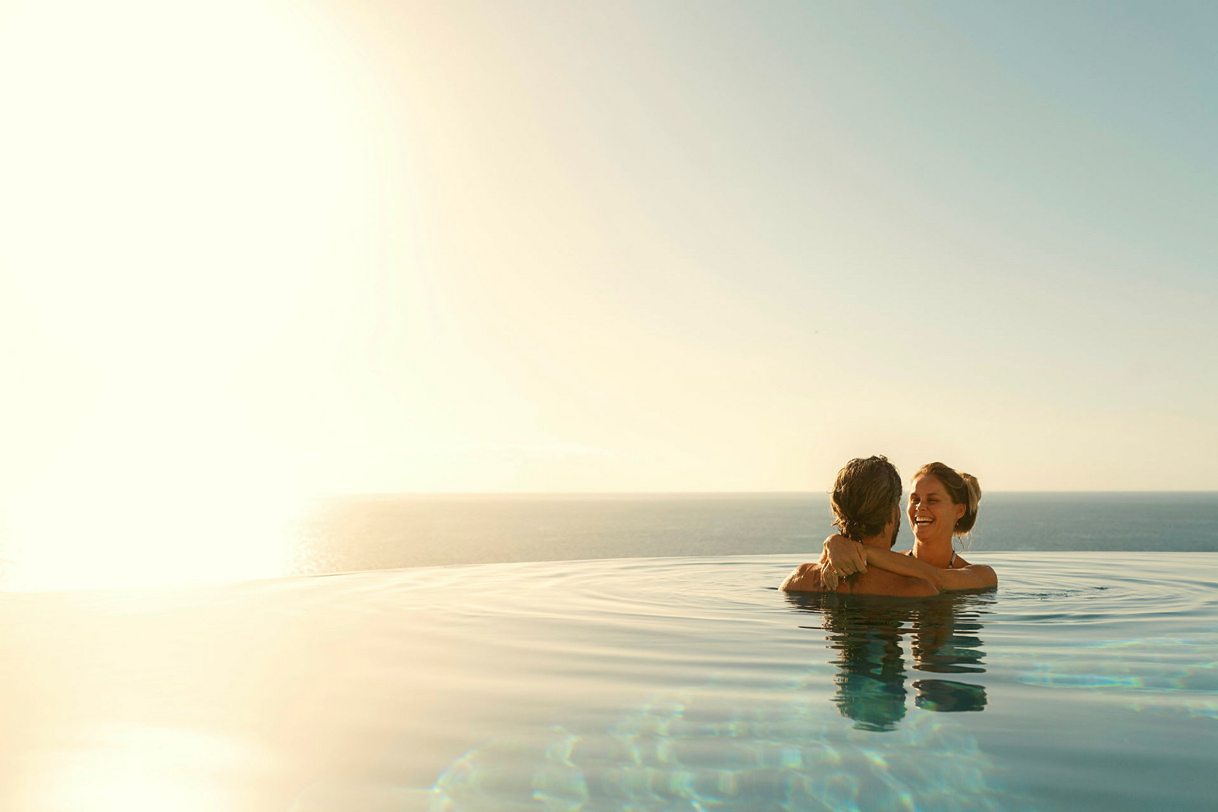 Två personer håller om varandra i en infinitypool med havsutsikt under en klar himmel. (AI-genererad text)