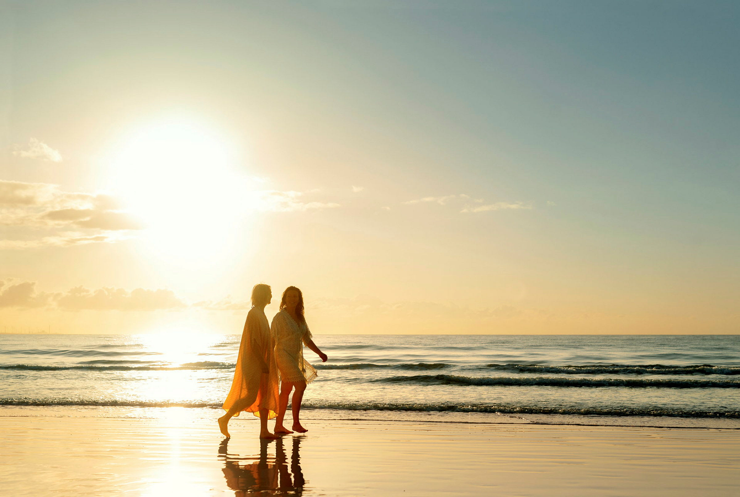 Två personer promenerar på en strand vid solnedgång. (AI-genererad text)