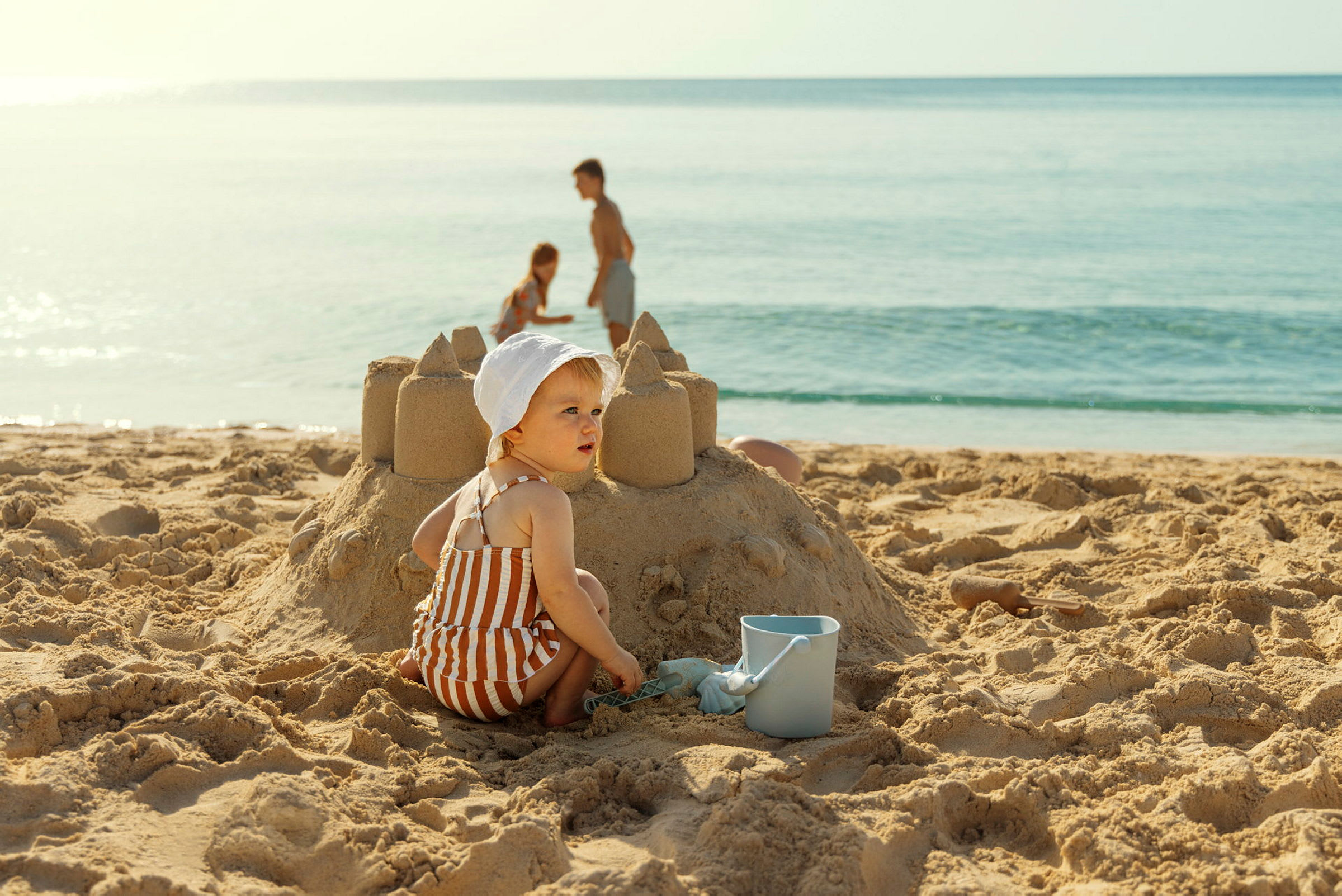 Barn som bygger ett sandslott på stranden med en hink bredvid. (AI-genererad text)