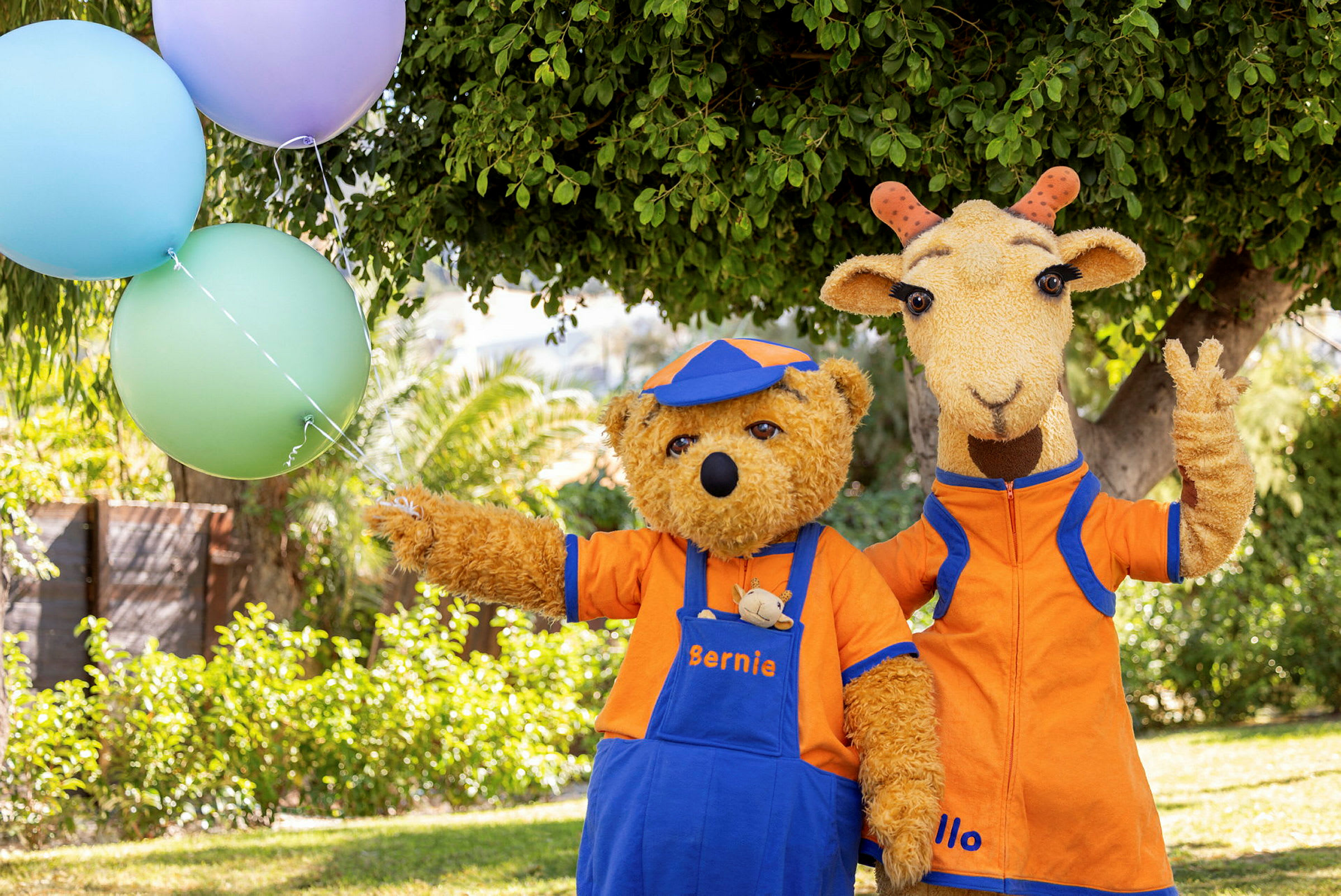 Två djurkaraktärer i orangea kläder står ute vid ett träd, med ballonger synliga till vänster. (AI-genererad text)
