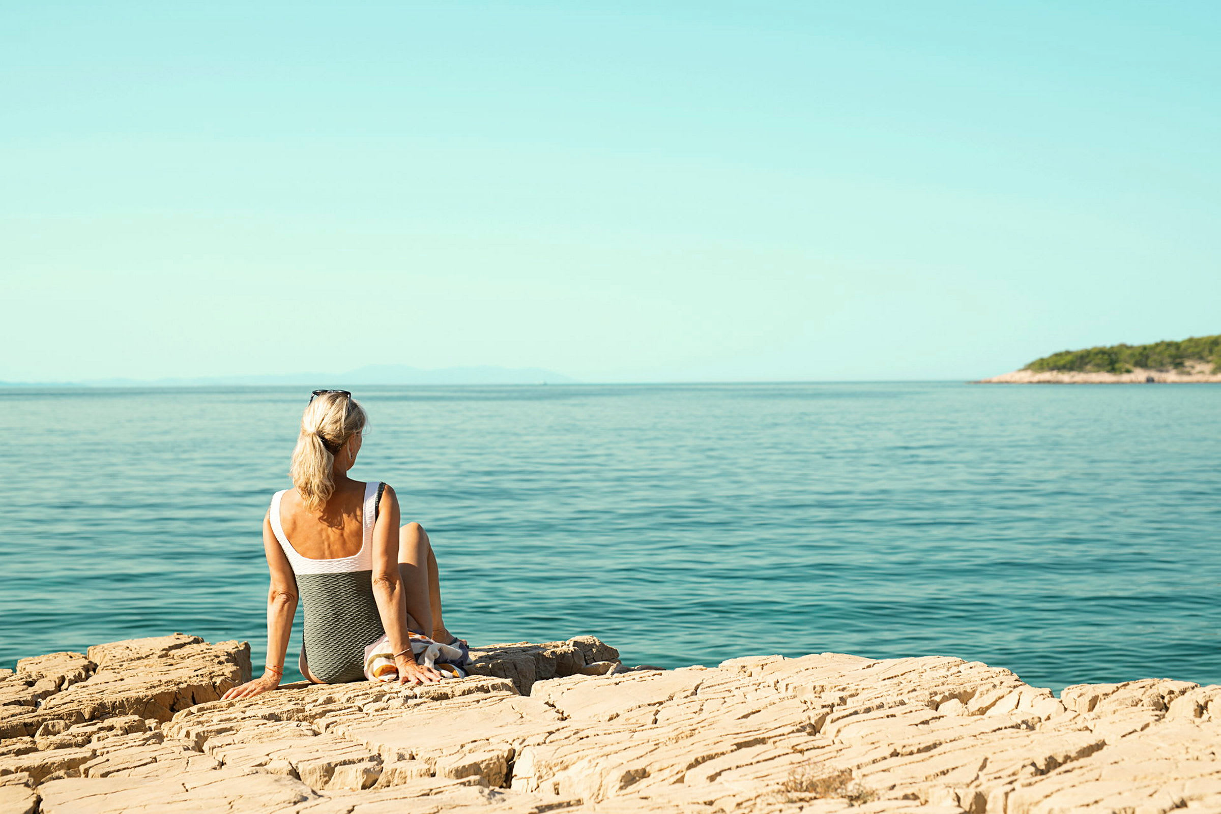En person sitter på en stenig kust och tittar mot havet. (AI-genererad text)