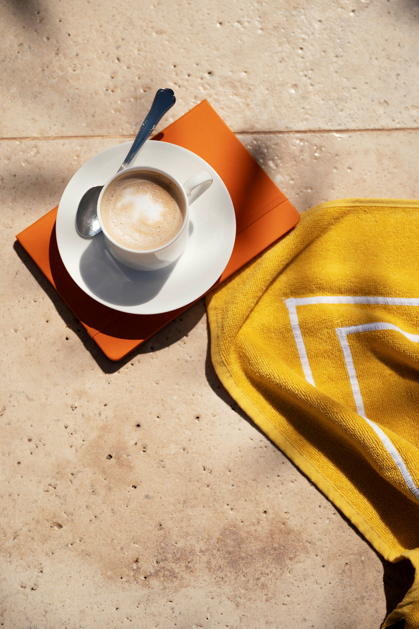 En kopp kaffe med en sked ligger på en fat med en orange bok och en gul handduk. (AI-genererad text)