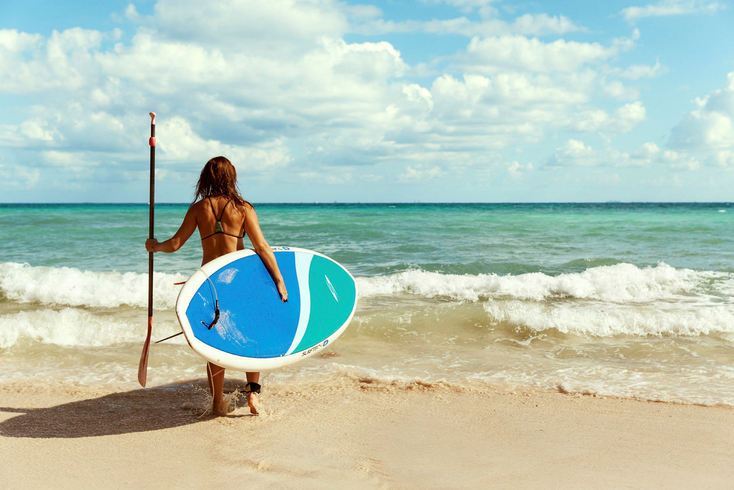 Person med våtdräkt och paddleboard på väg mot havet. (AI-genererad text)