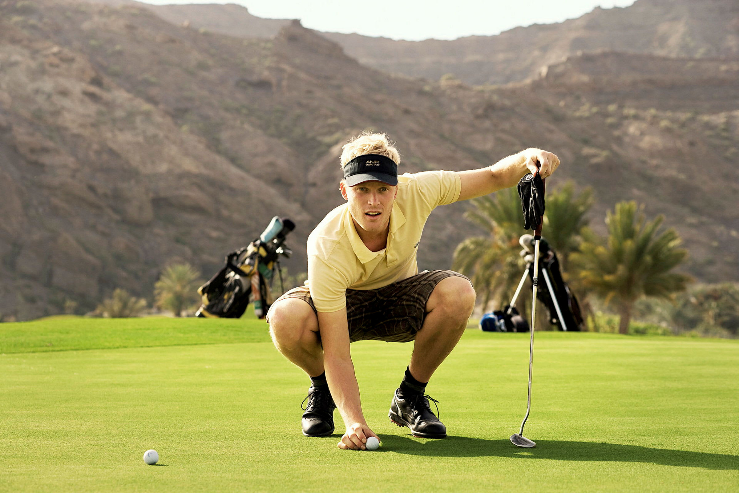 Person placerar golfboll på green med berg i bakgrunden. (AI-genererad text)