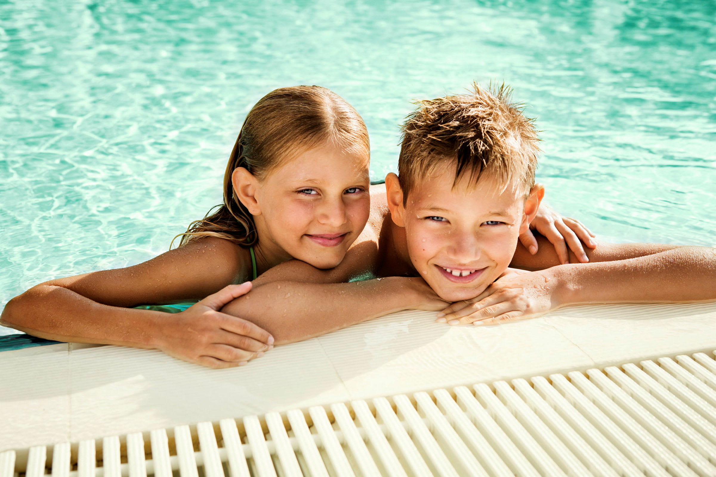 Två personer ligger vid kanten av en pool med vattnet i bakgrunden. (AI-genererad text)