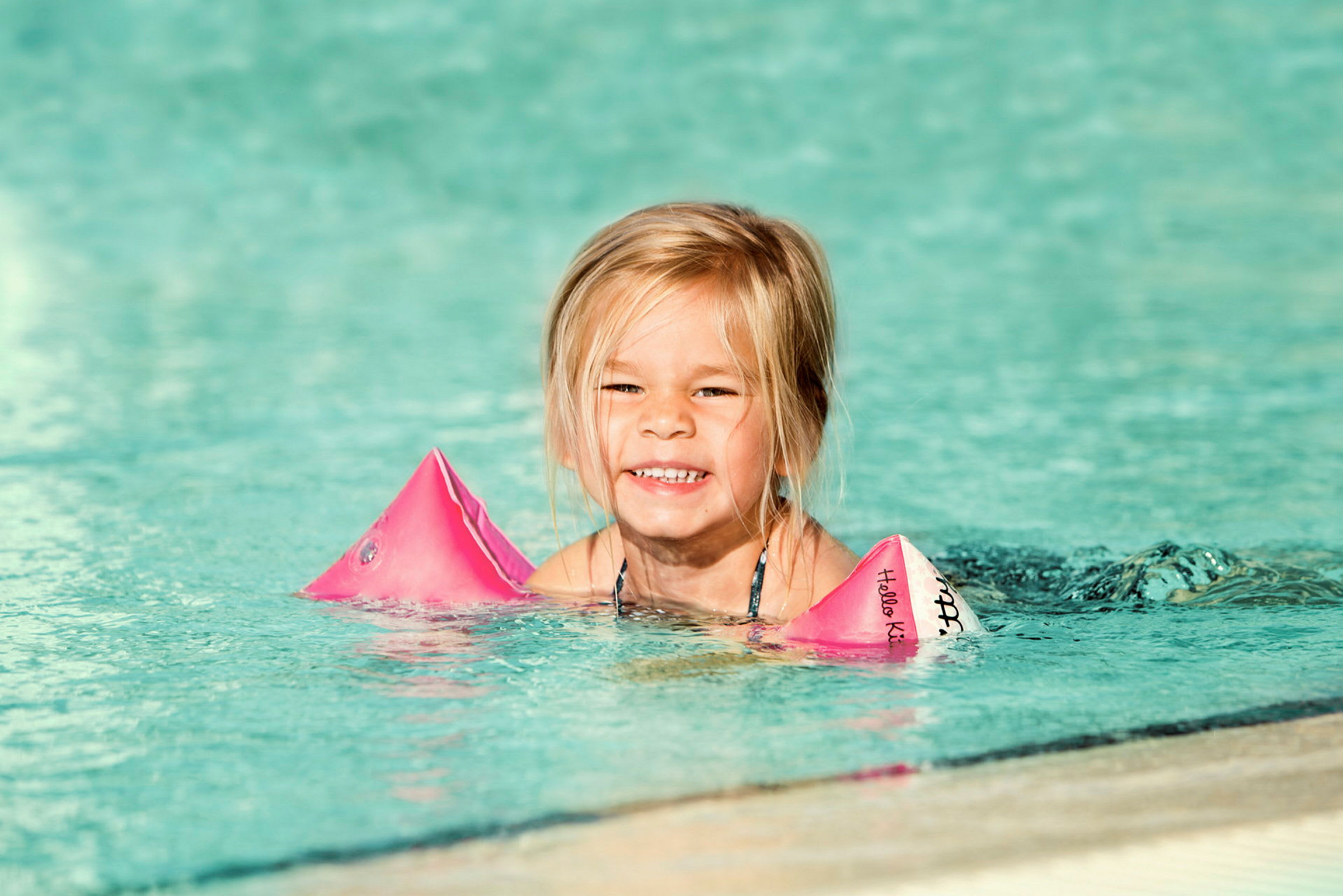 Ett barn i en pool med rosa simdynor på armarna. (AI-genererad text)