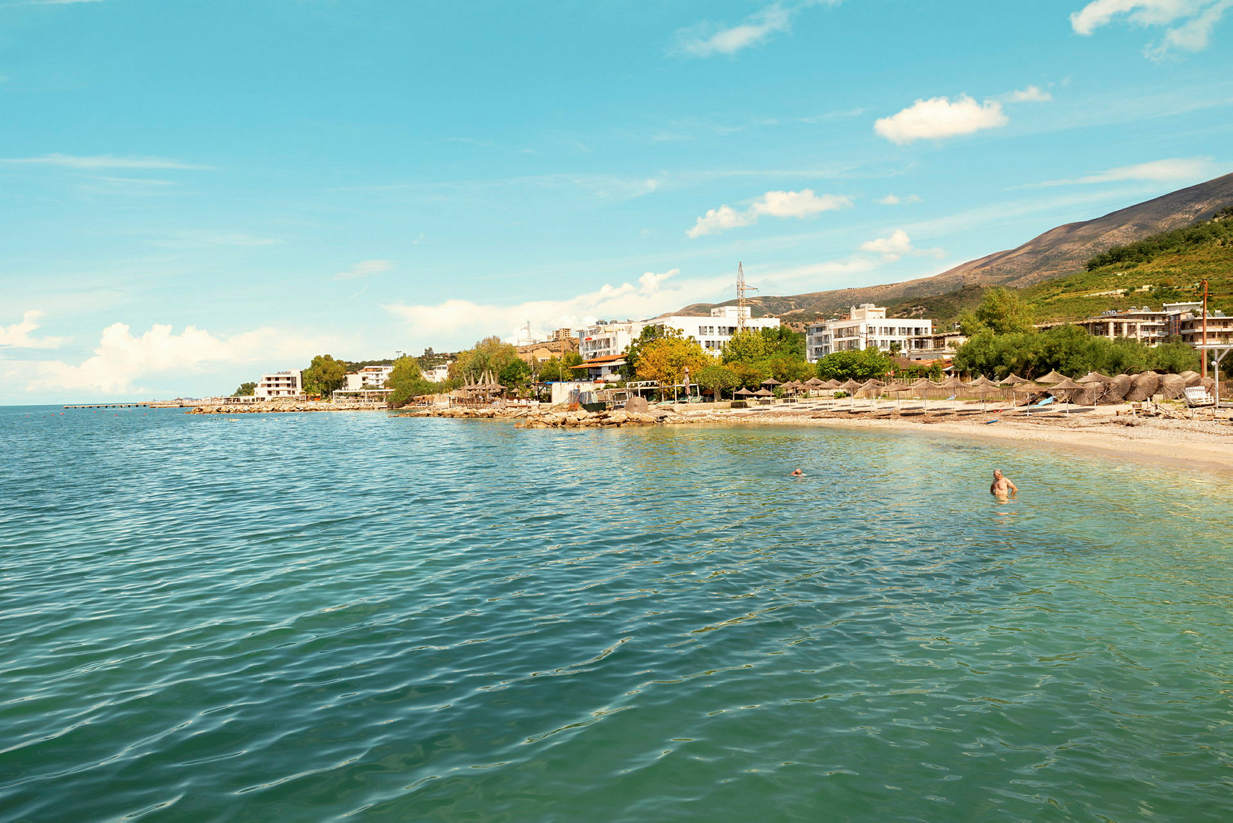 En strand med klart vatten och byggnader i bakgrunden. (AI-genererad text)