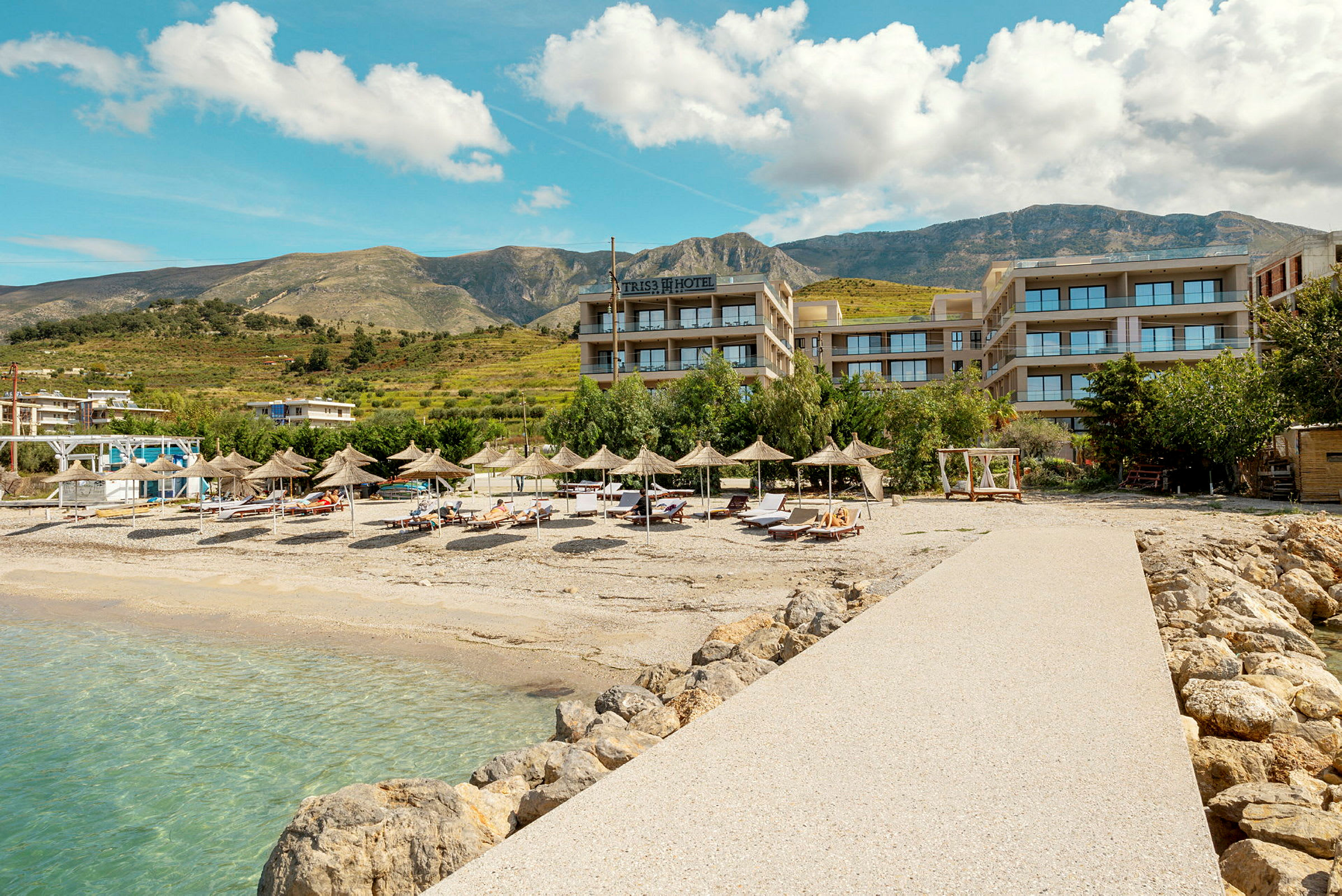 Hotellvy vid en stenig strand med parasoller och solsängar. (AI-genererad text)