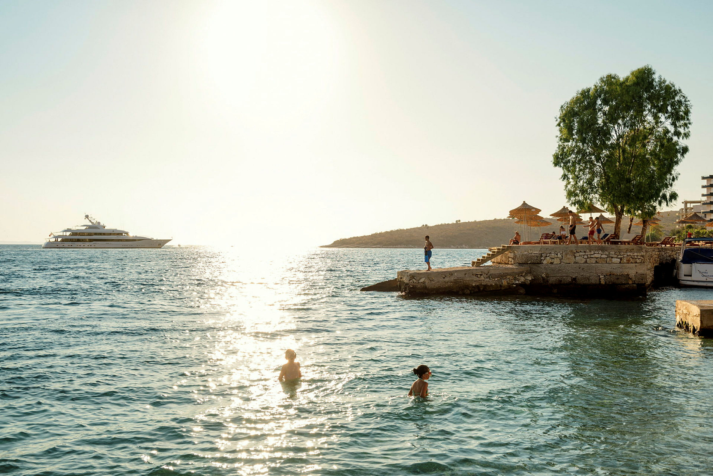 Människor simmar i havet nära en brygga med solstolar och parasoller. (AI-genererad text)