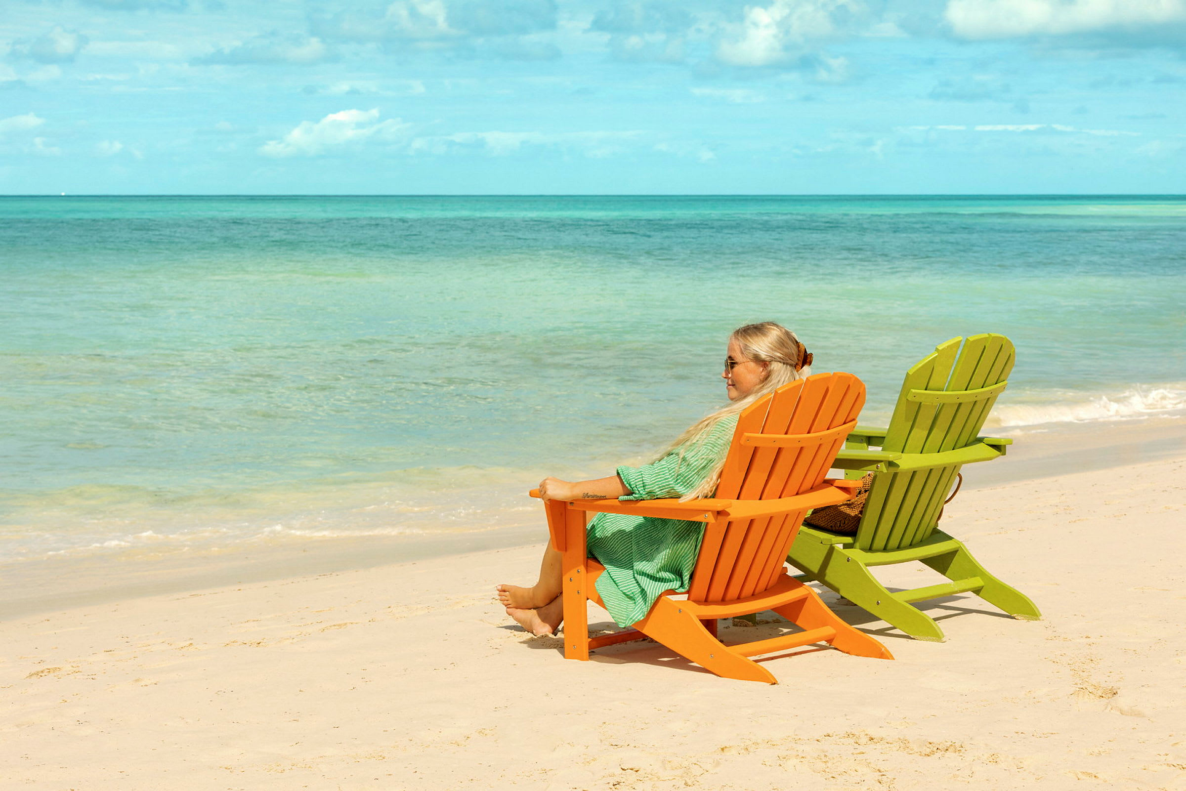Två solstolar, en orange och en grön, står på en sandstrand med havet i bakgrunden. (AI-genererad text)