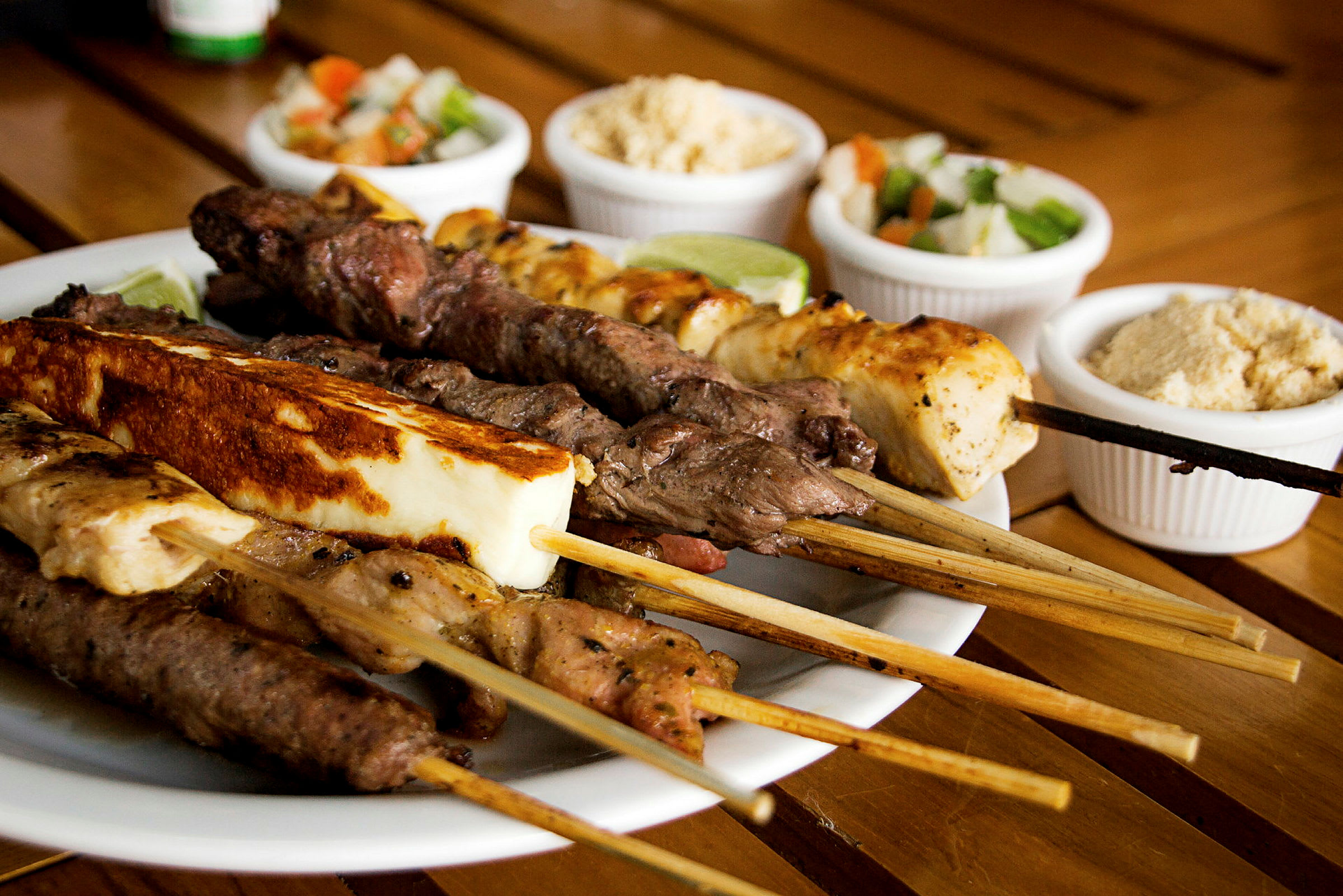 En tallrik med grillspett av olika typer av kött och ost, med små skålar av tillbehör i bakgrunden. (AI-genererad text)