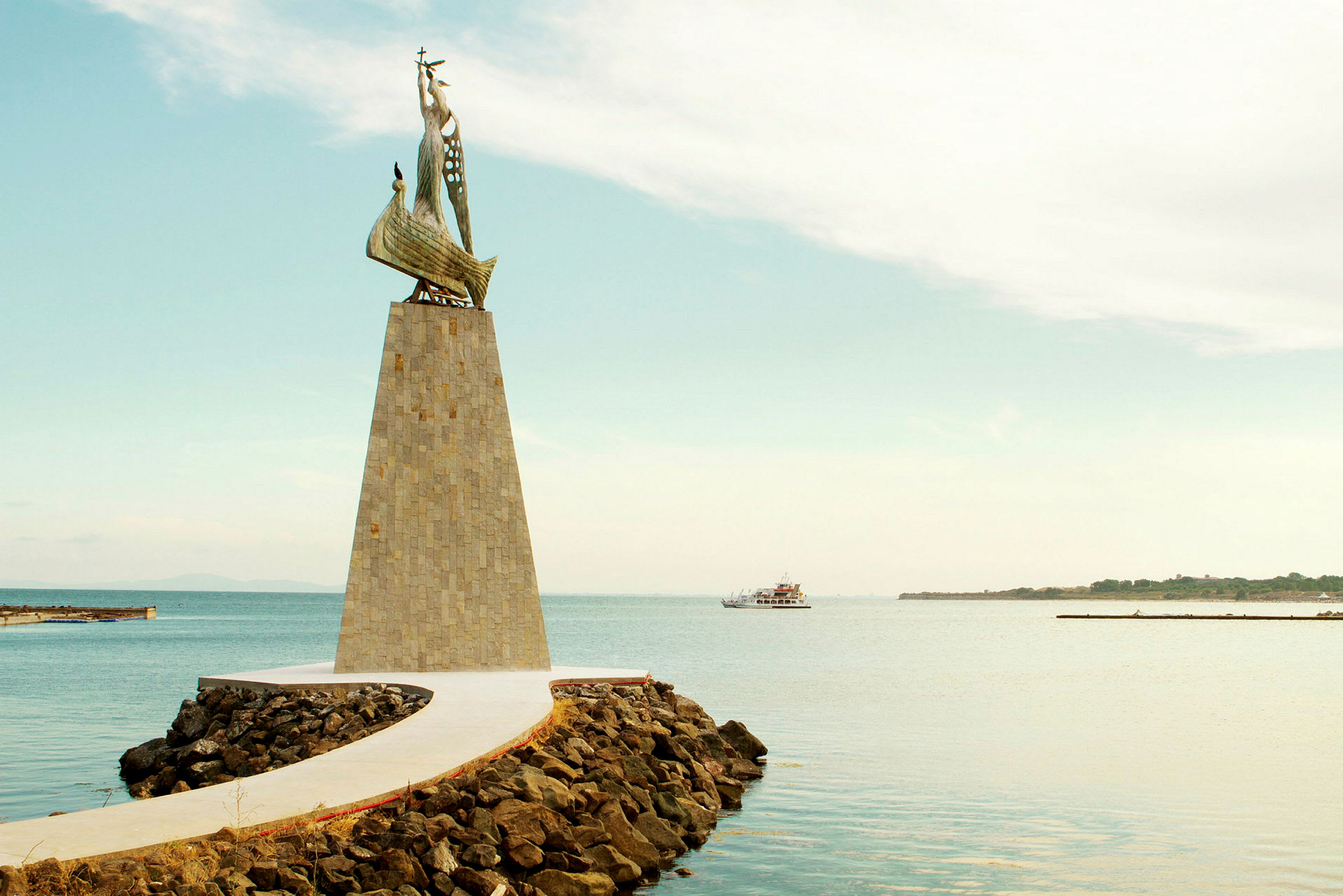 Ett monument med en skulptur av ett skepp, beläget vid en brygga omgiven av vatten. (AI-genererad text)