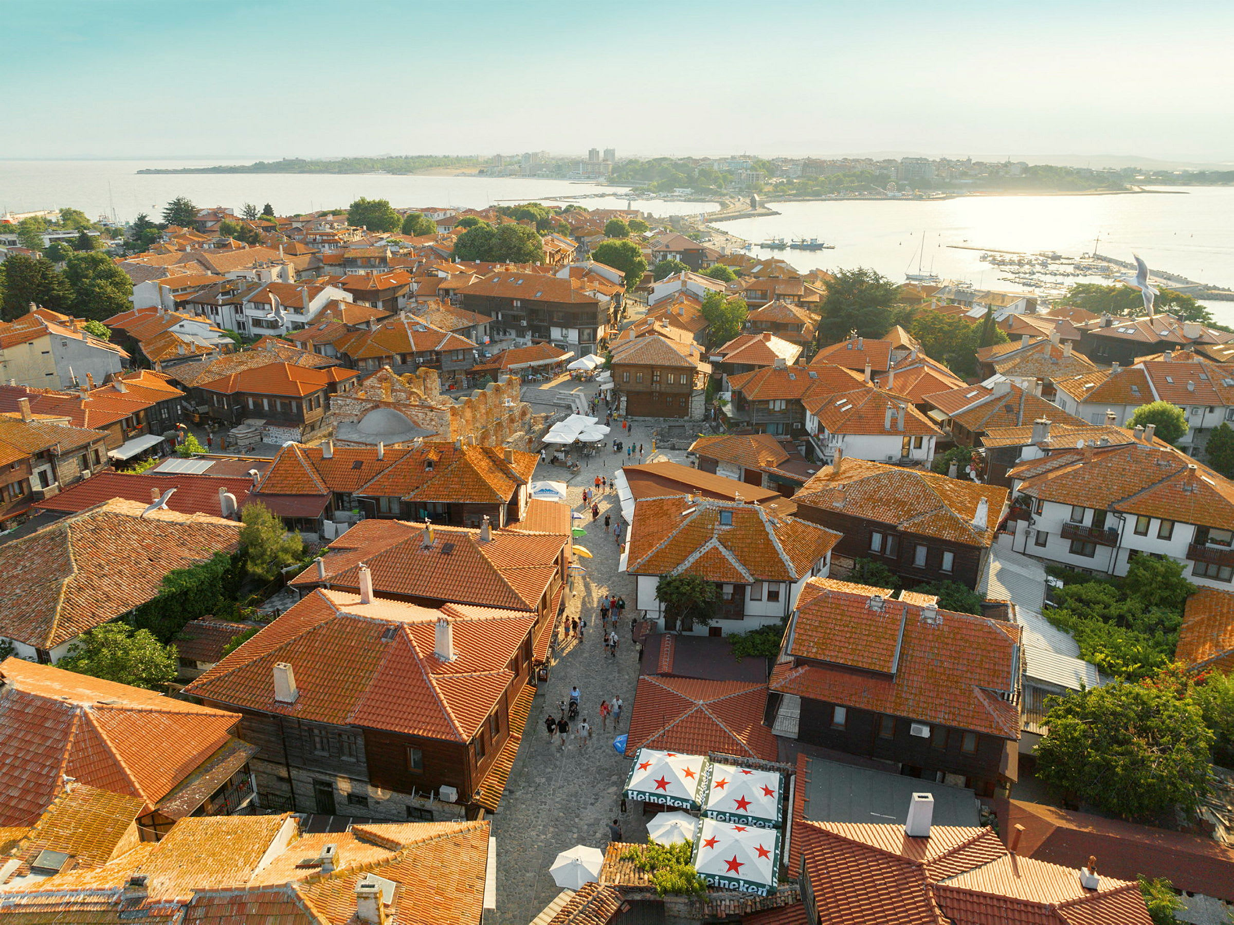 Luftvy över en stad med många hus med röda tak, kullerstensgator och gröna träd. (AI-genererad text)