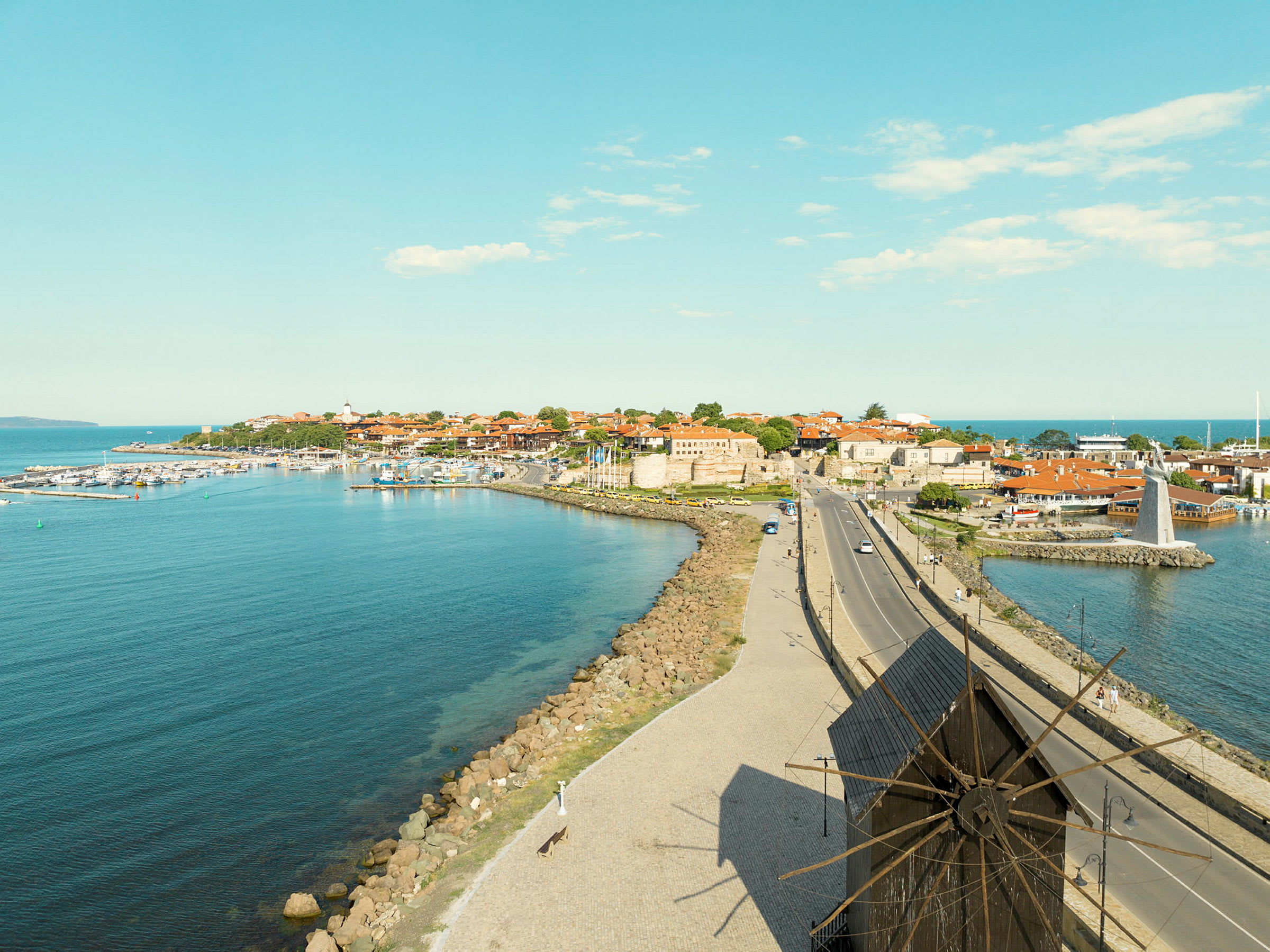En kuststad med byggnader, en vindmölla och en väg i förgrunden. (AI-genererad text)