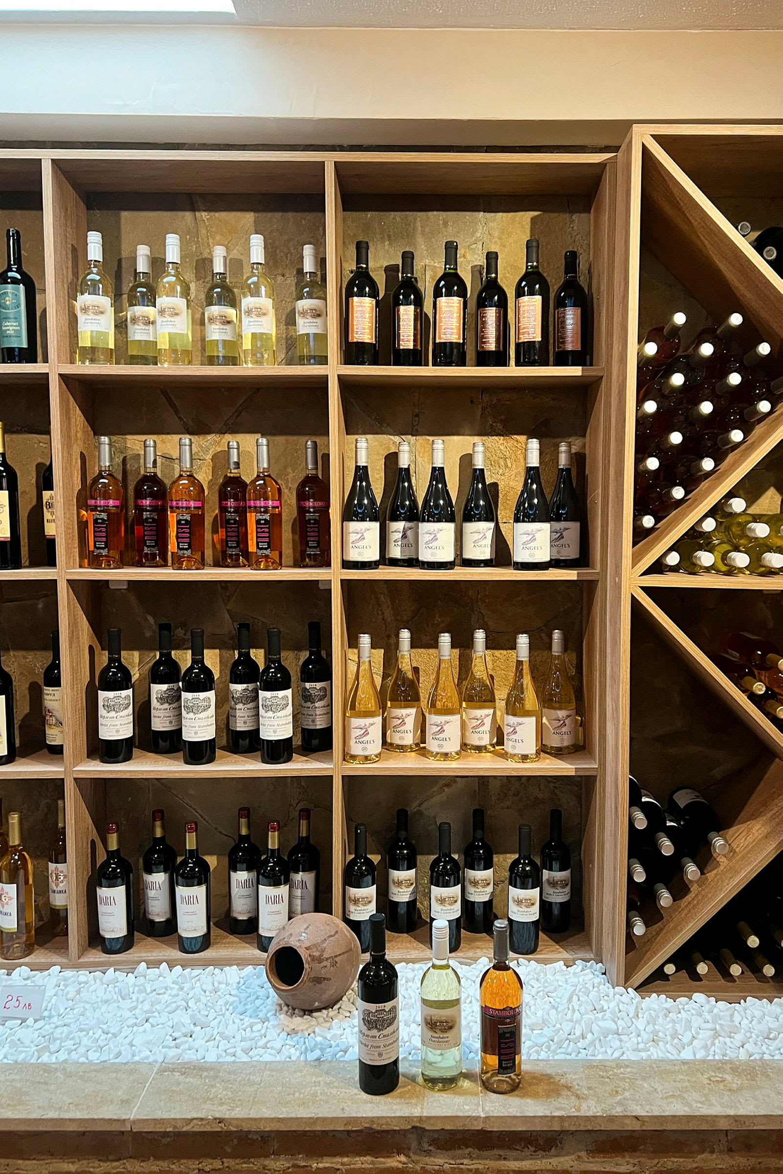En vägg med hyllor fyllda med flaskor av vin i olika färger och sorter. (AI-genererad text)