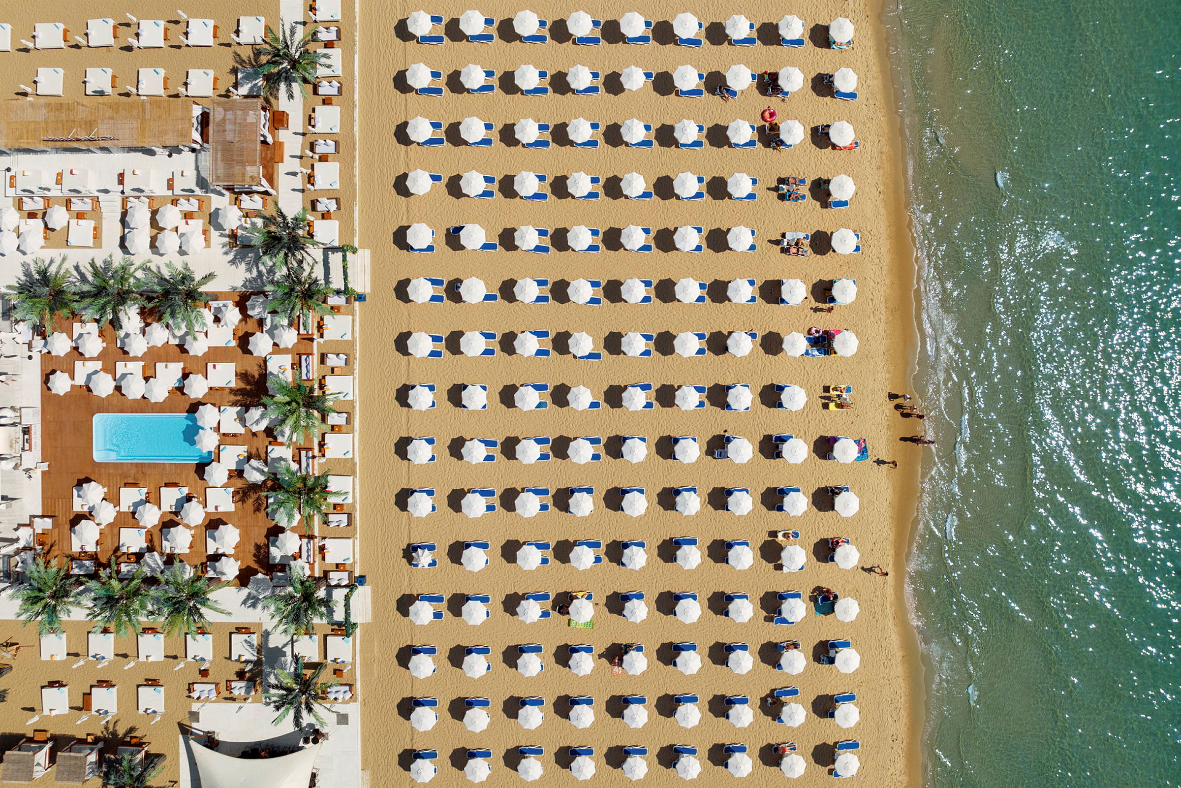 Luftvy av en strand med ordnade parasoller och solbäddar nära vattnet. (AI-genererad text)