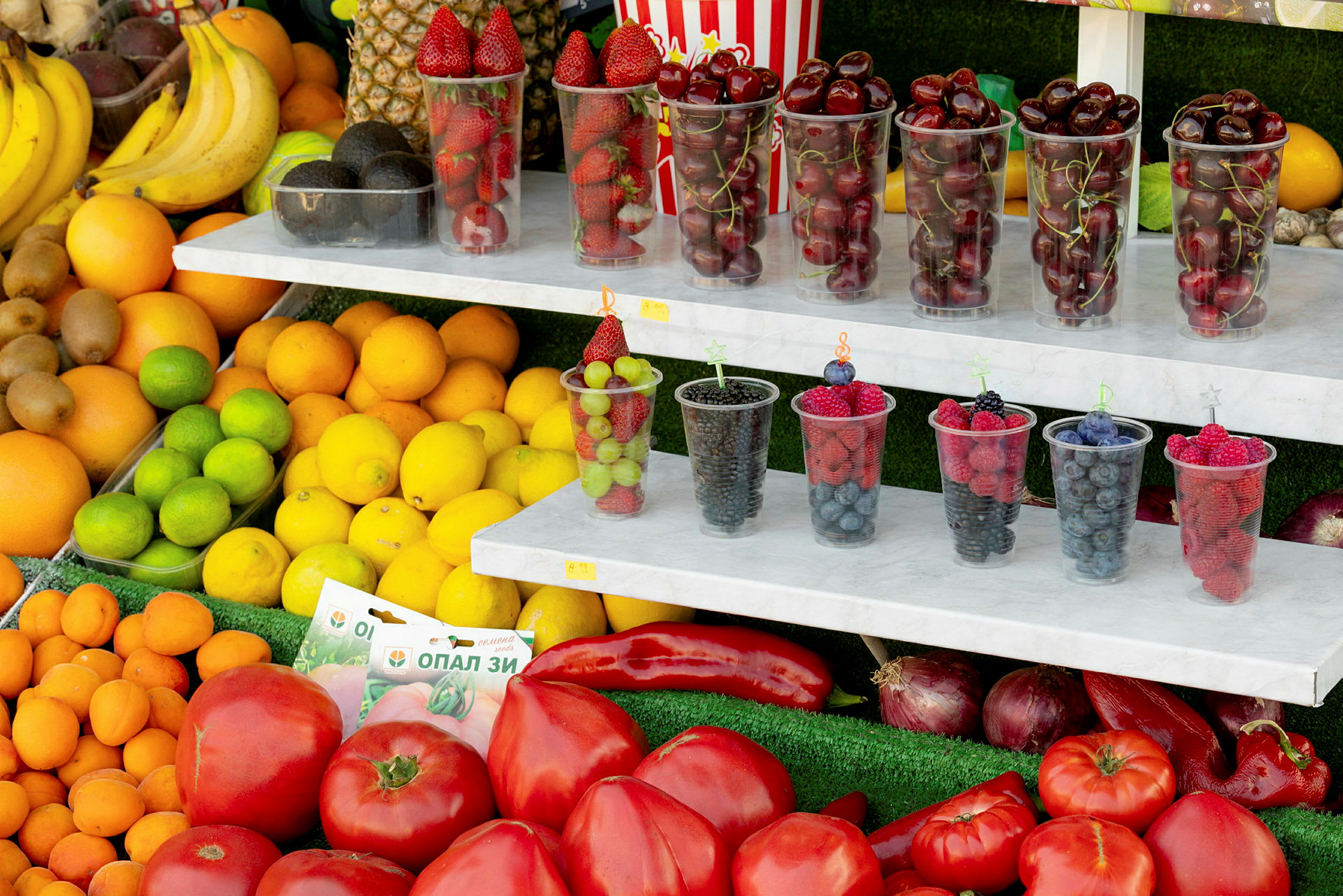 Olika frukter och grönsaker, samt plastmuggar fyllda med färska bär. (AI-genererad text)