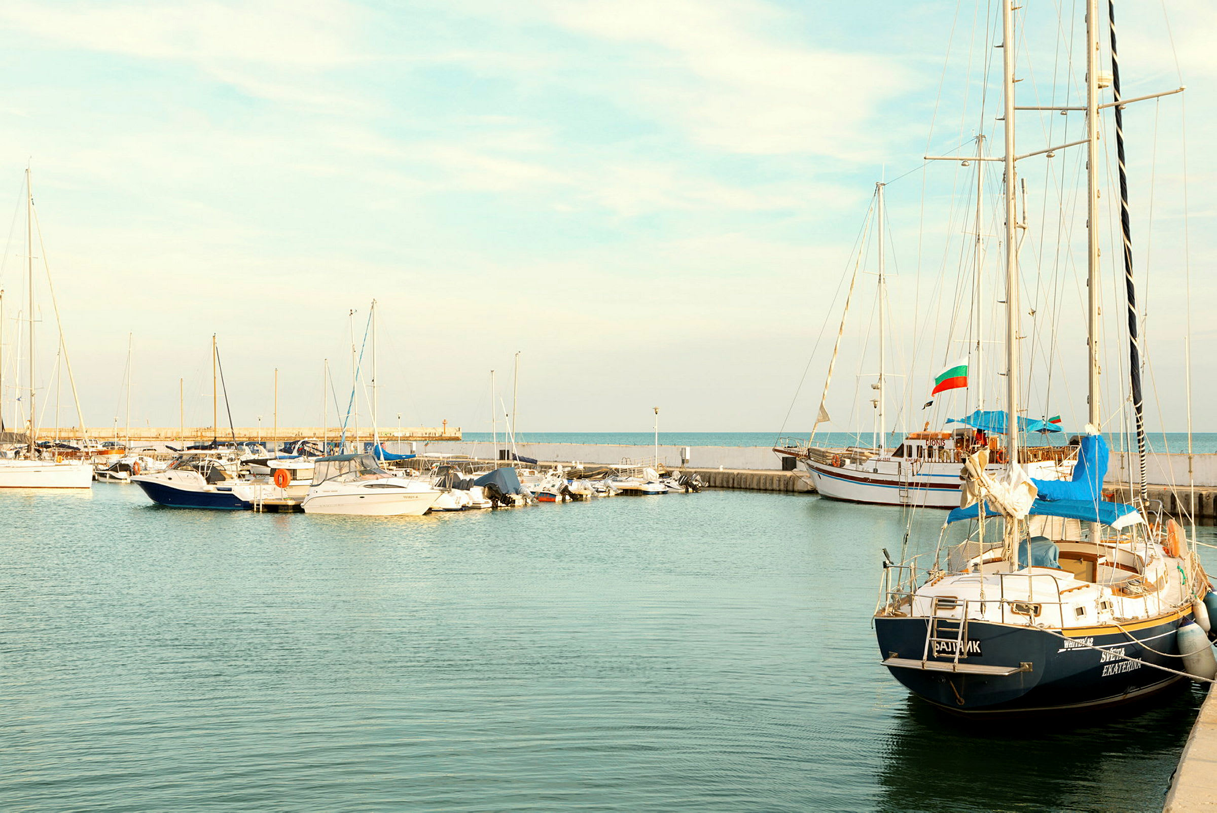 Småbåtar och segelfartyg förtöjda i hamnen, med havet i bakgrunden. (AI-genererad text)
