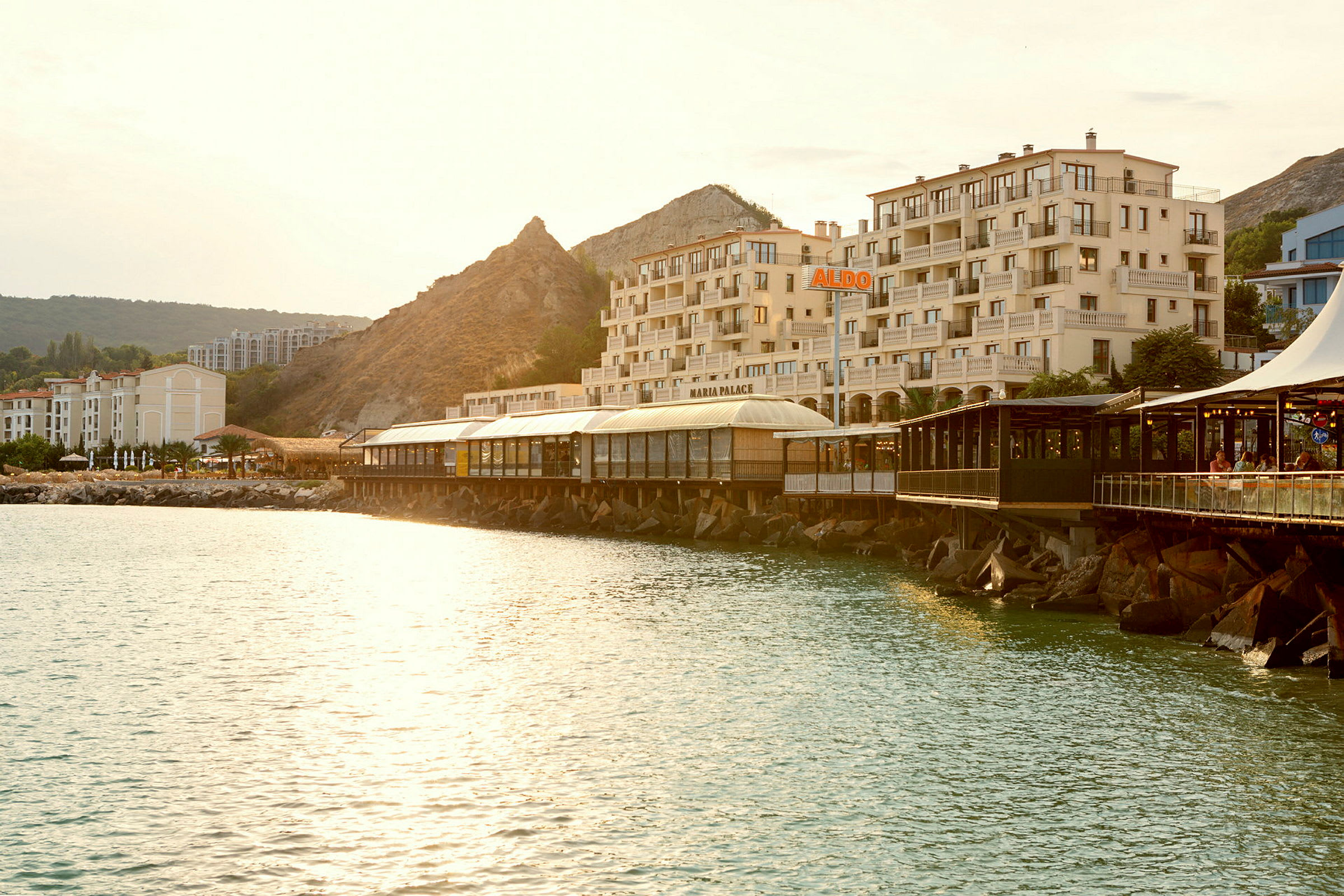 Vy över en kust med vatten, byggnader och en restaurang på en brygga. (AI-genererad text)
