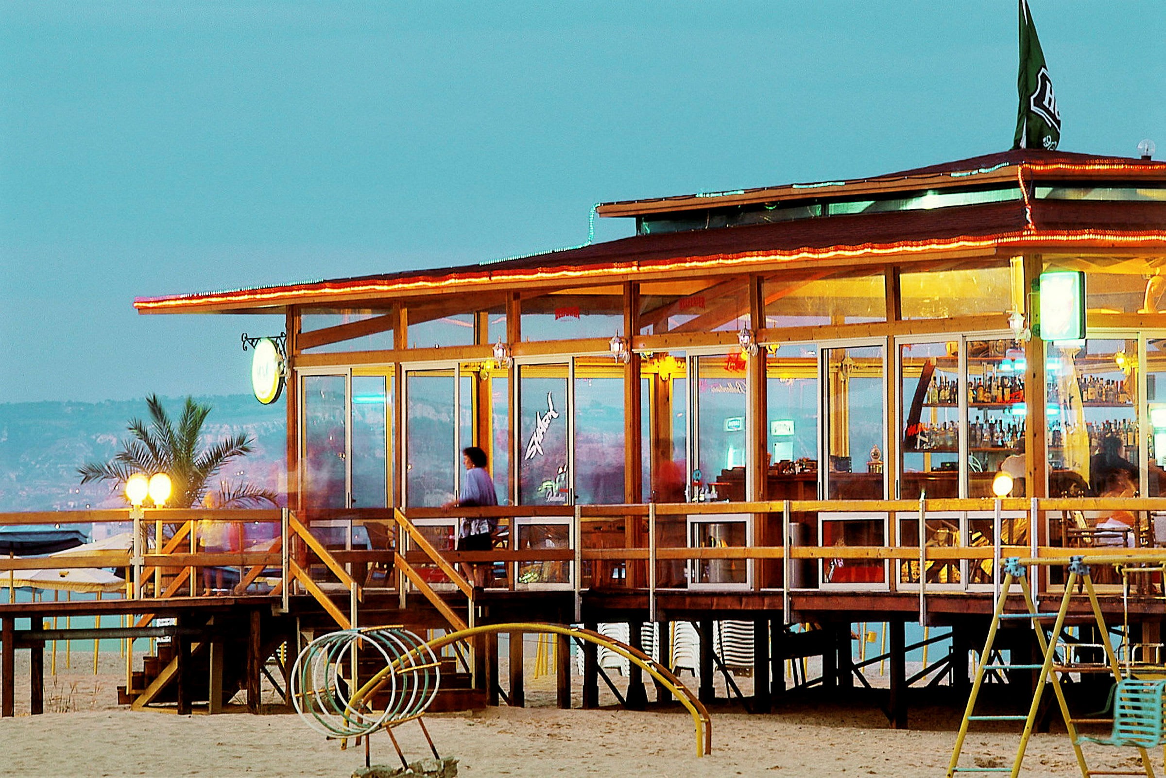En strandbar med träkonstruktion och glasväggar på kvällen. (AI-genererad text)