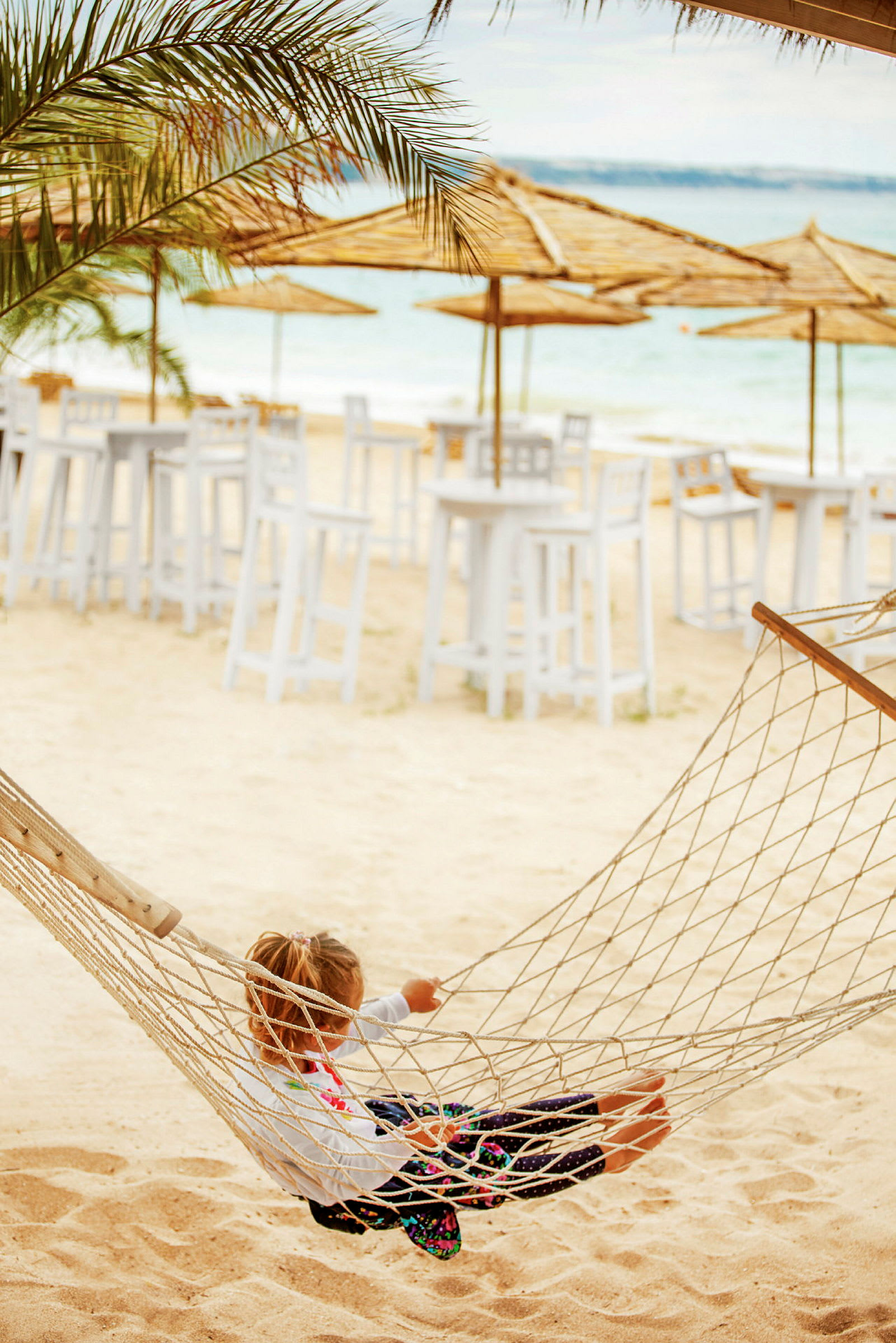 Ett barn som sitter i en hängmatta på en sandstrand. (AI-genererad text)