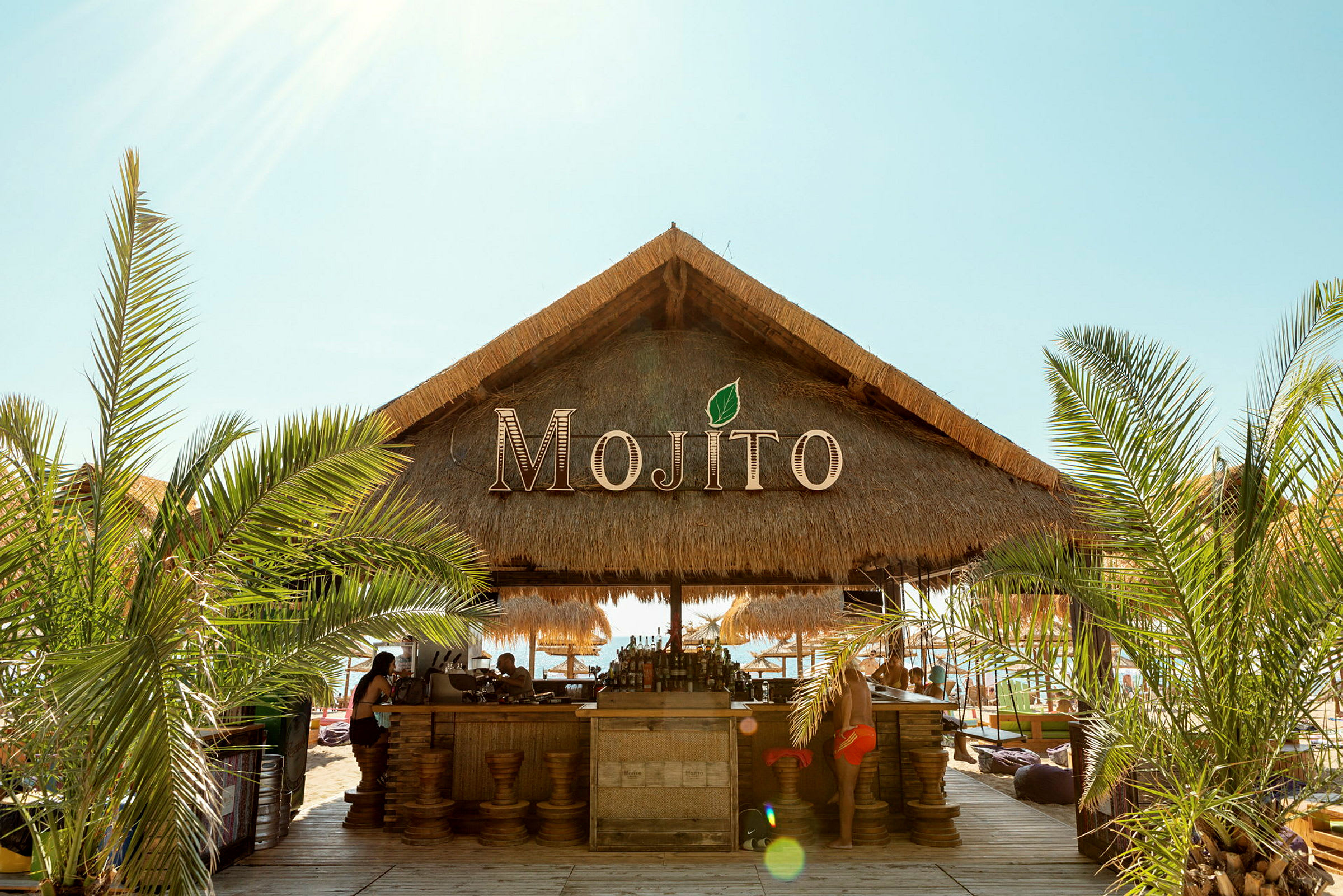 En strandbar med halmtak och namnet Mojito. (AI-genererad text)