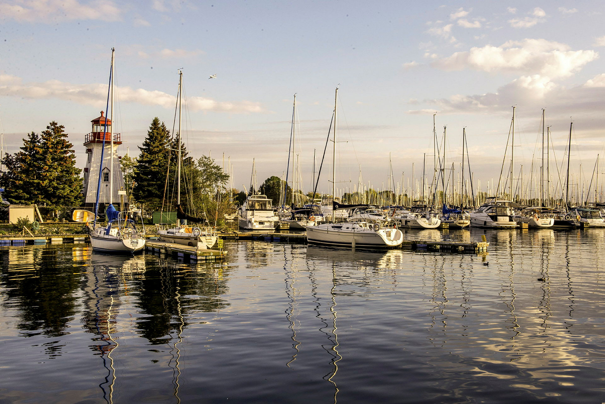 Bilden visar en småbåtshamn med en fyr och flera segelbåtar som ligger förtöjda vid bryggan. (AI-genererad text)