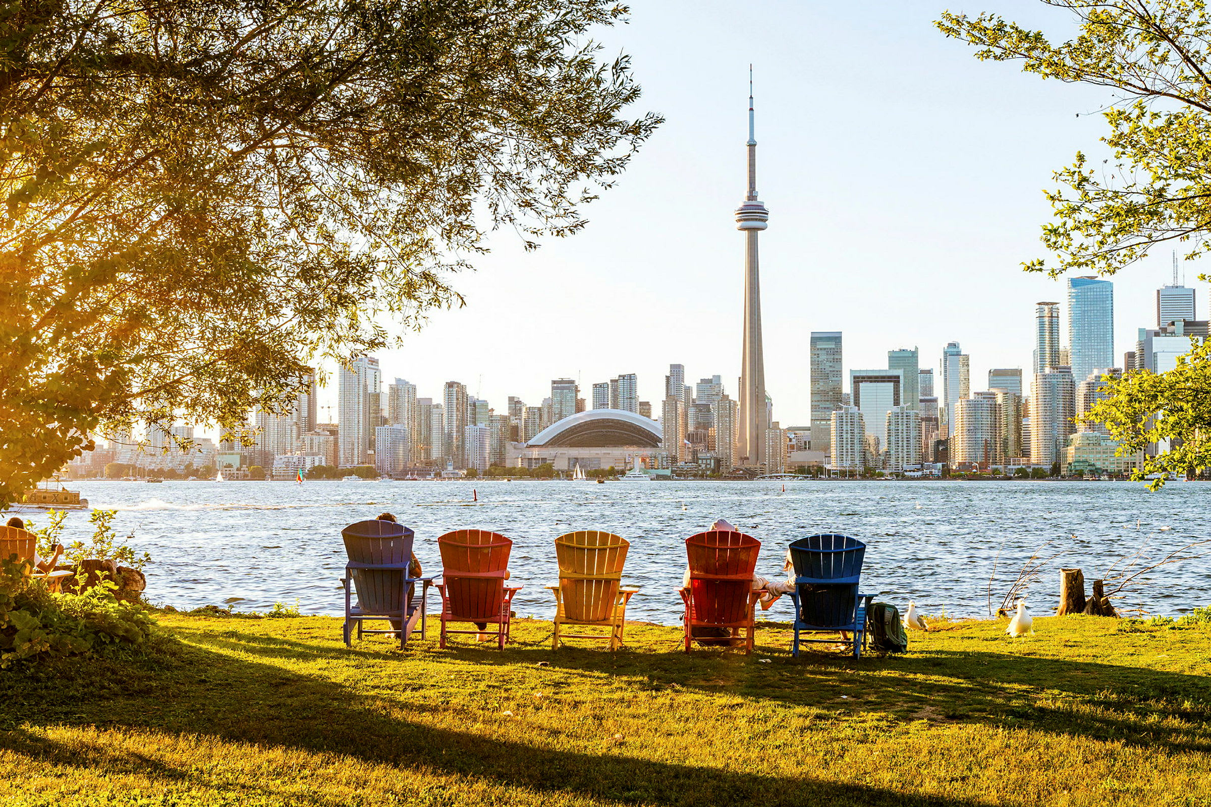 Färgade stolar vid en park med utsikt över en stadssiluett och CN Tower. (AI-genererad text)
