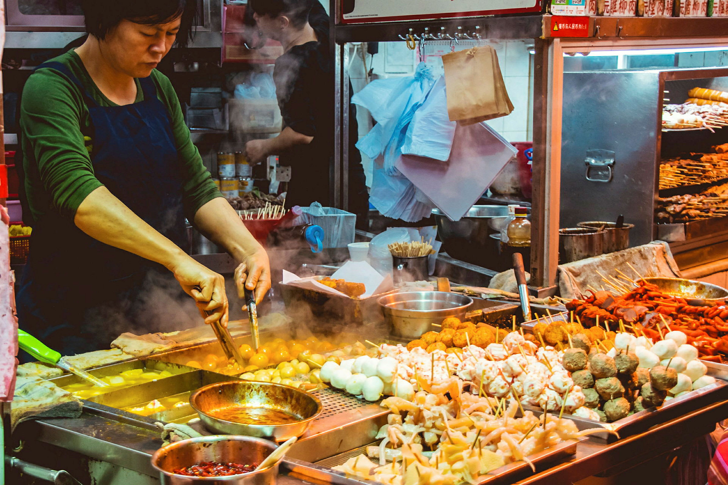 En matförsäljare tillagar street food över en varm stekyta i ett livligt matstånd. (AI-genererad text)