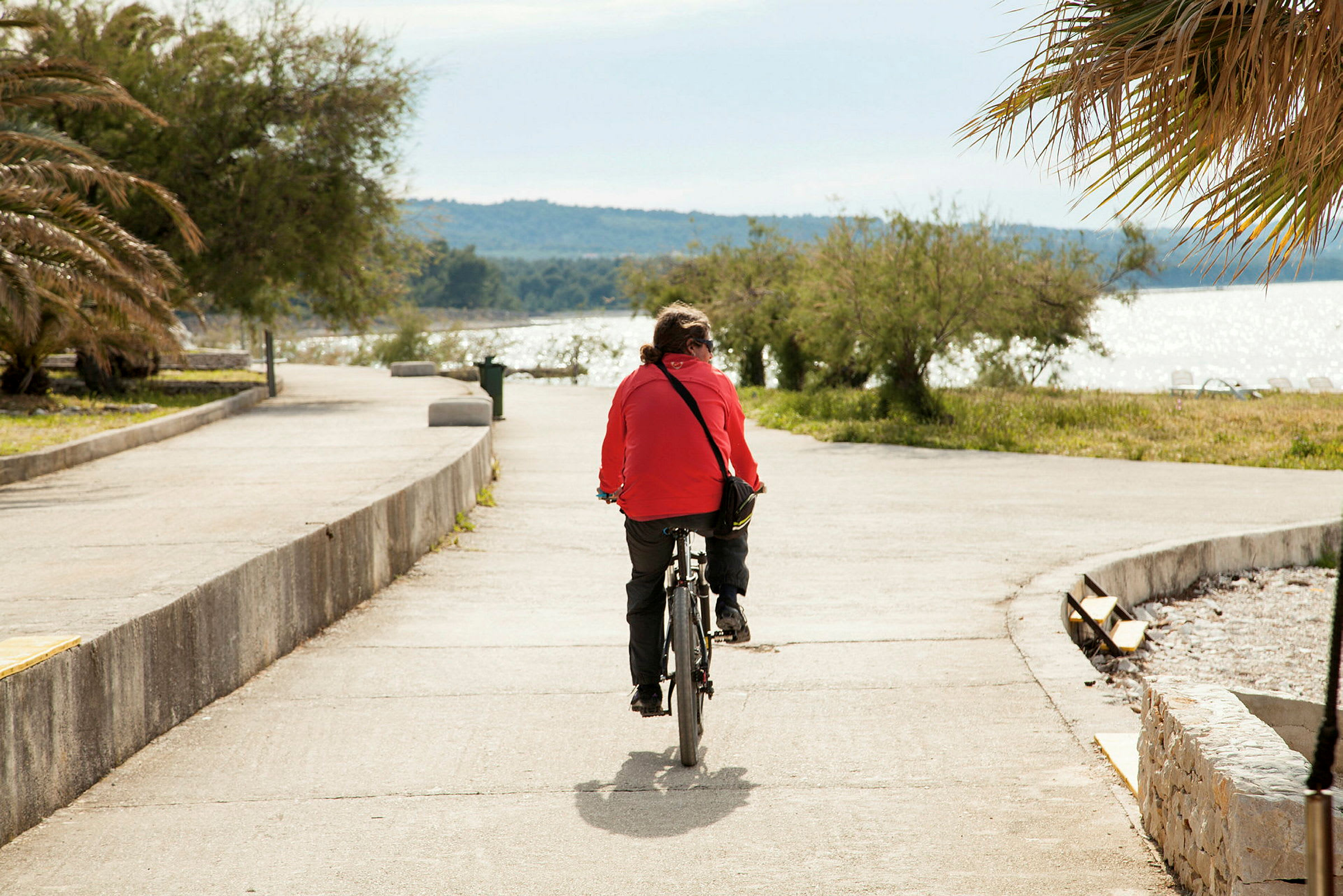 En person cyklar vid en havspromenad med träd och palmer i bakgrunden. (AI-genererad text)