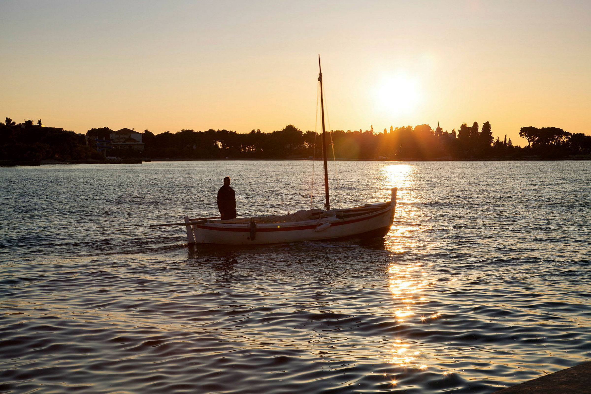 Man står på liten båt i vatten vid solnedgång. (AI-genererad text)