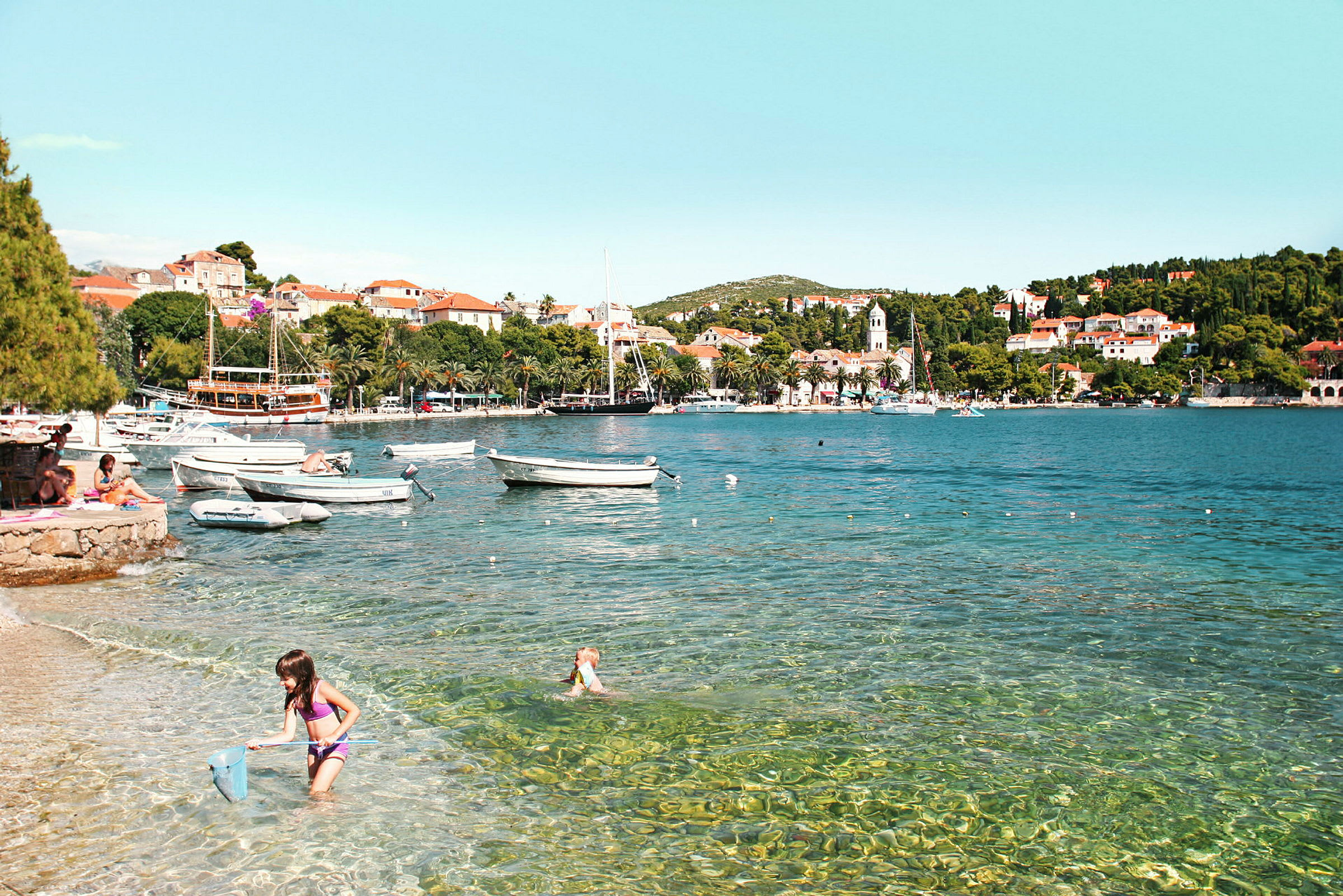 Strand med klart vatten, småbåtar och en stad i bakgrunden. (AI-genererad text)
