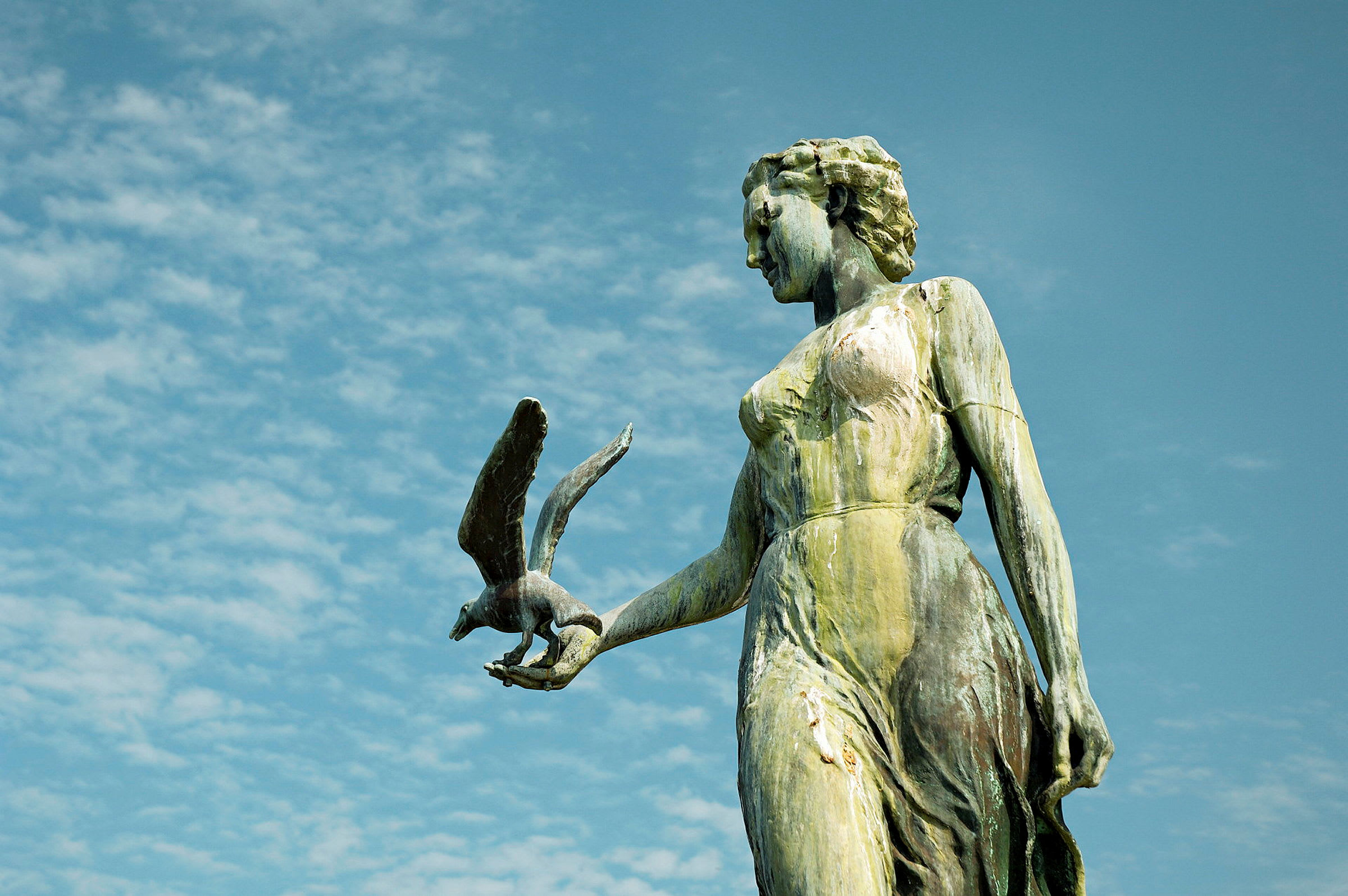 Staty av en kvinna med en fågel i handen mot en blå himmel. (AI-genererad text)