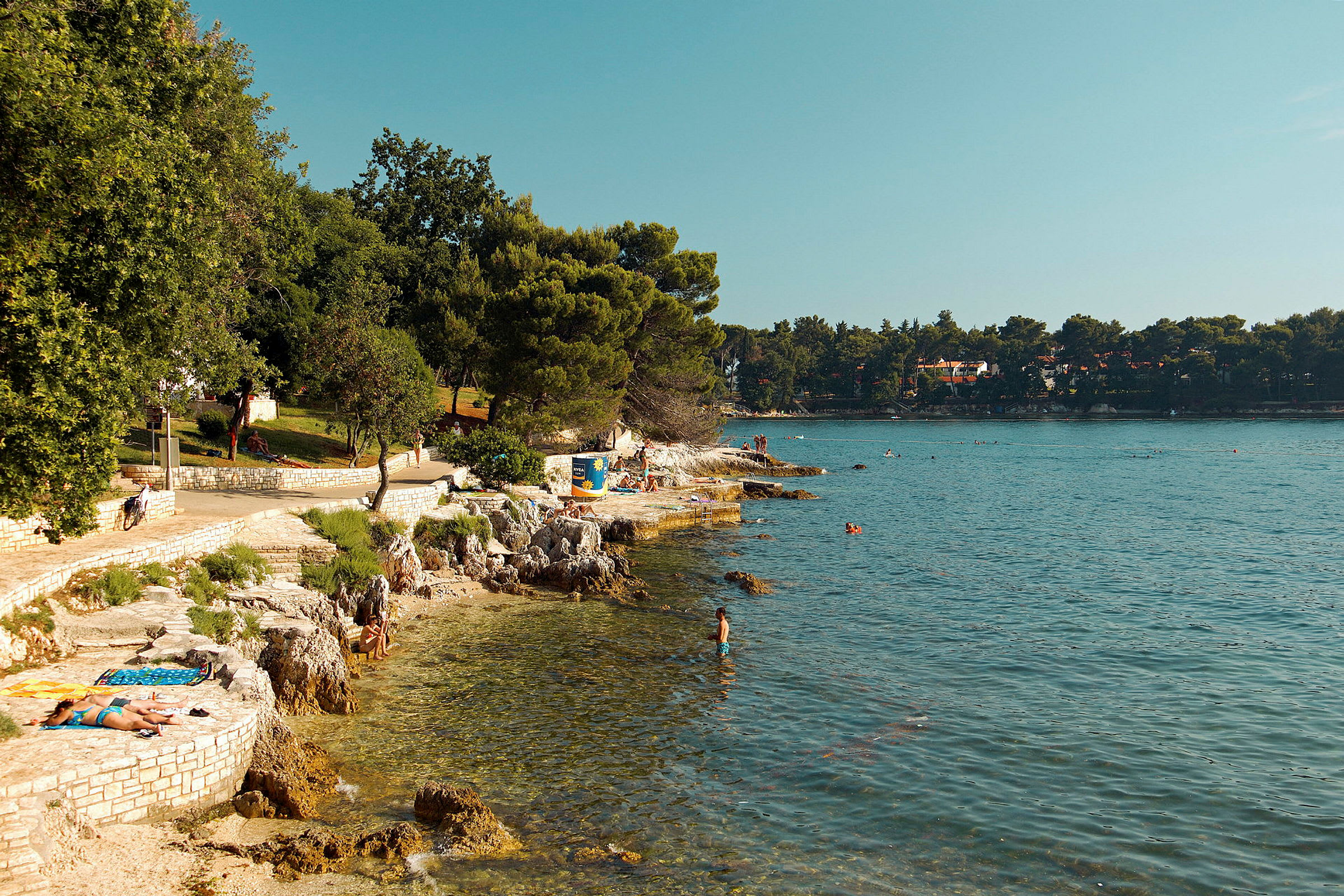 Kuststräcka vid havet med människor som solar och badar. (AI-genererad text)