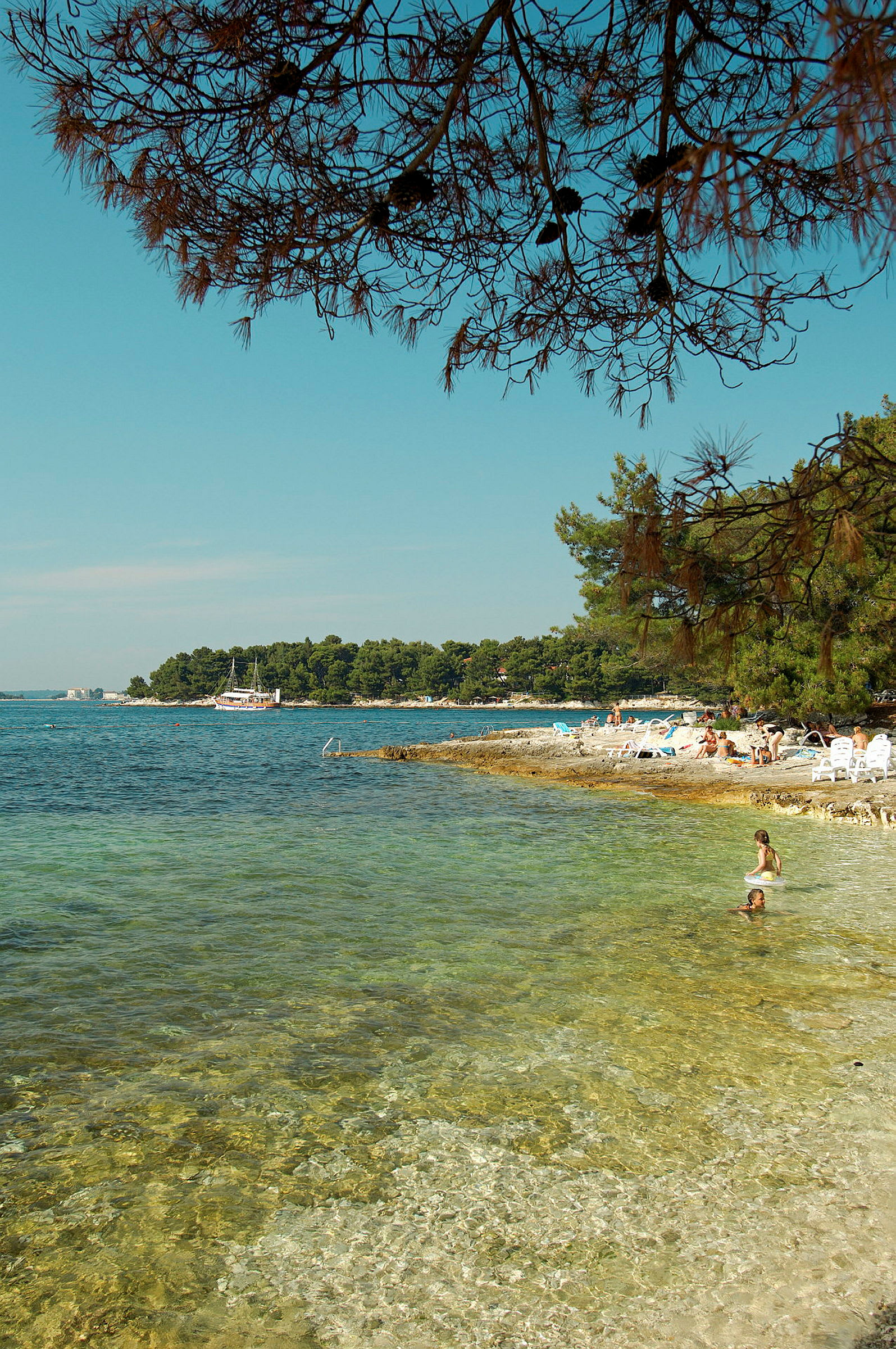 Strand med klara vatten och människor som badar, omgiven av träd och en båt längre bort. (AI-genererad text)