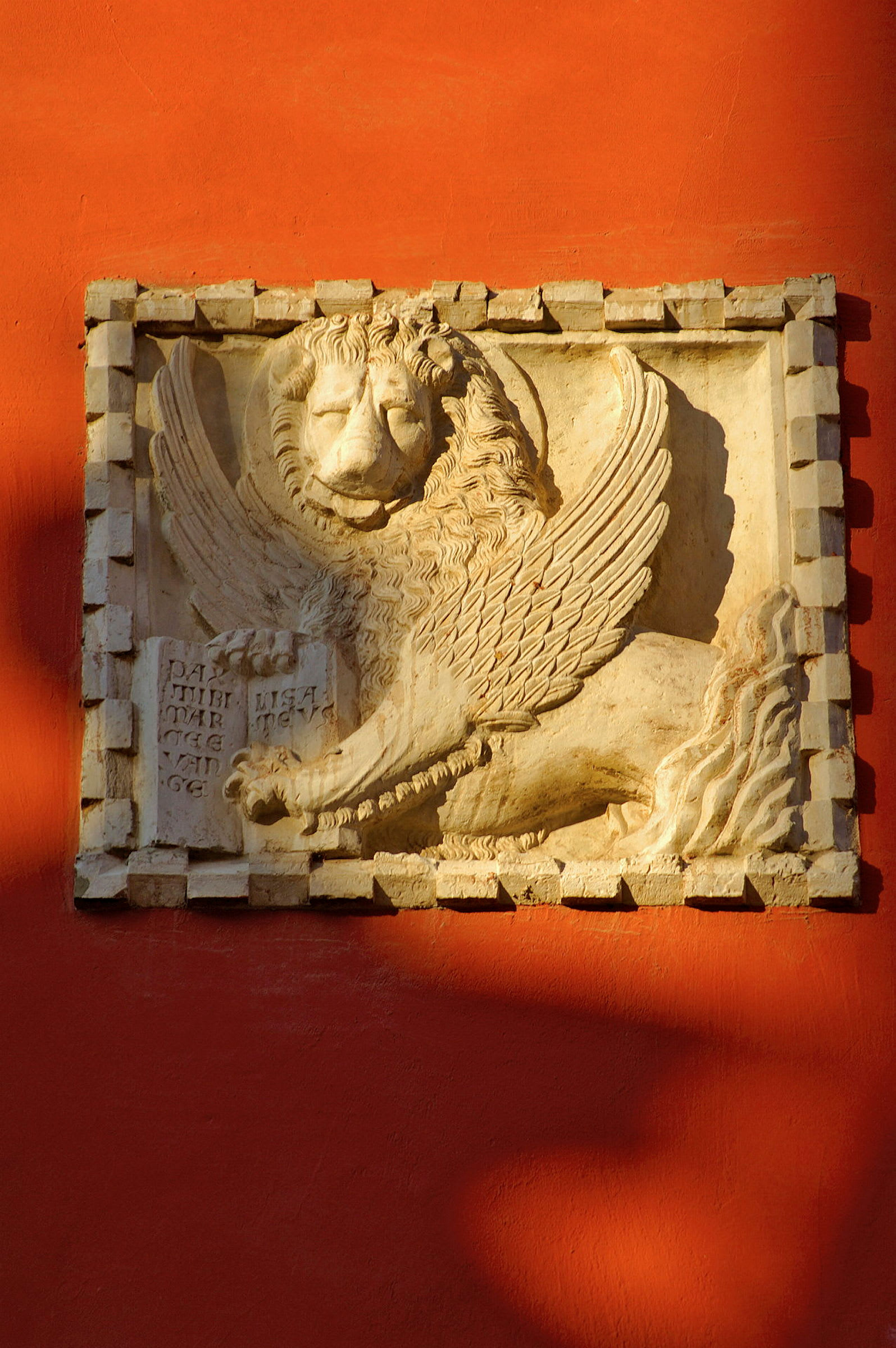 Relief av en bevingad lejonfigur på en röd vägg. (AI-genererad text)